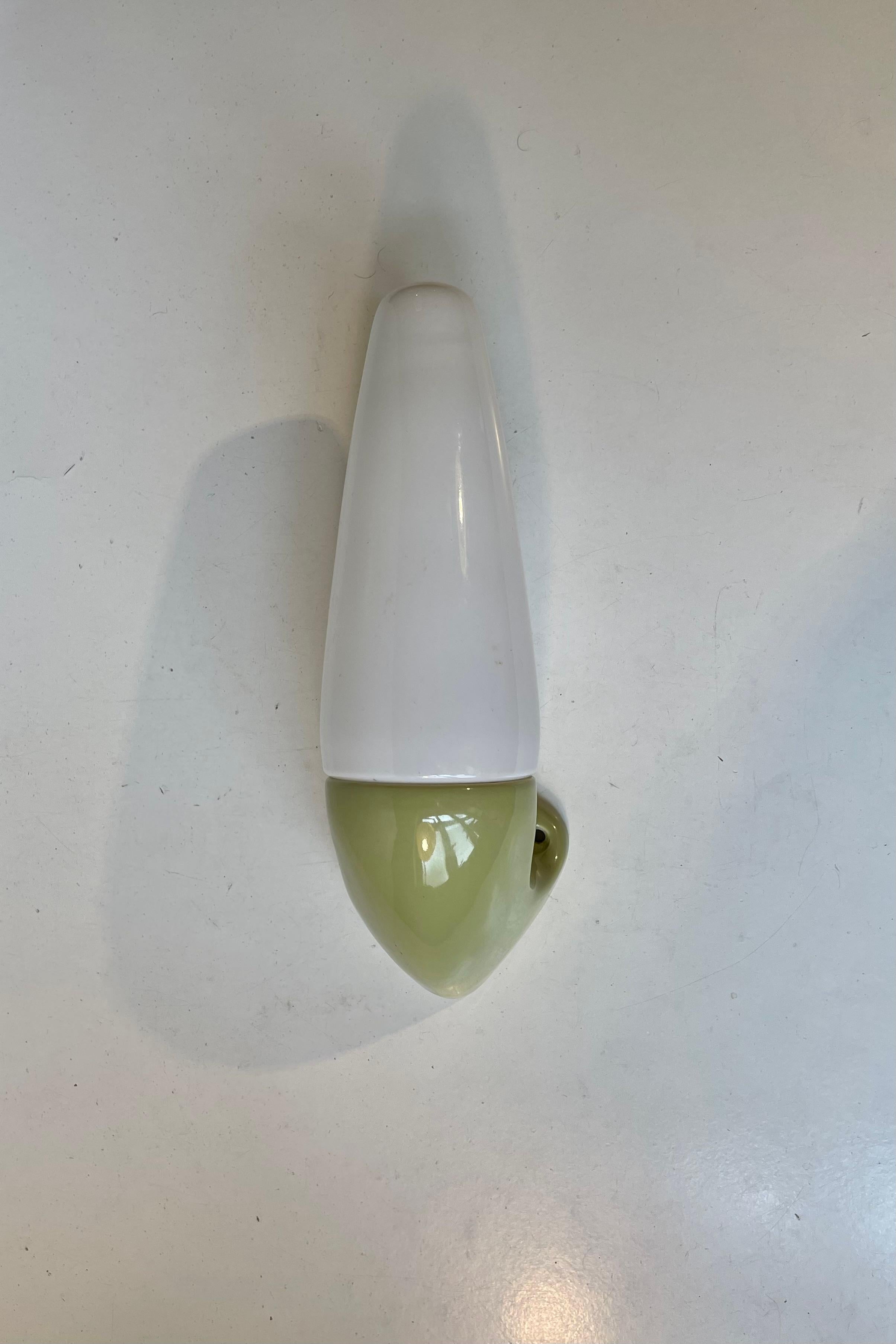 Wall sconce suitable as bathroom or outdoor lighting. Designed by Royalty - Prince Sigvard Bernadotte for the swedish company Ifö during the 1960s. Green/light olive glazed porcelain mount with a white opaline glass shade. 2 way mount - either shade
