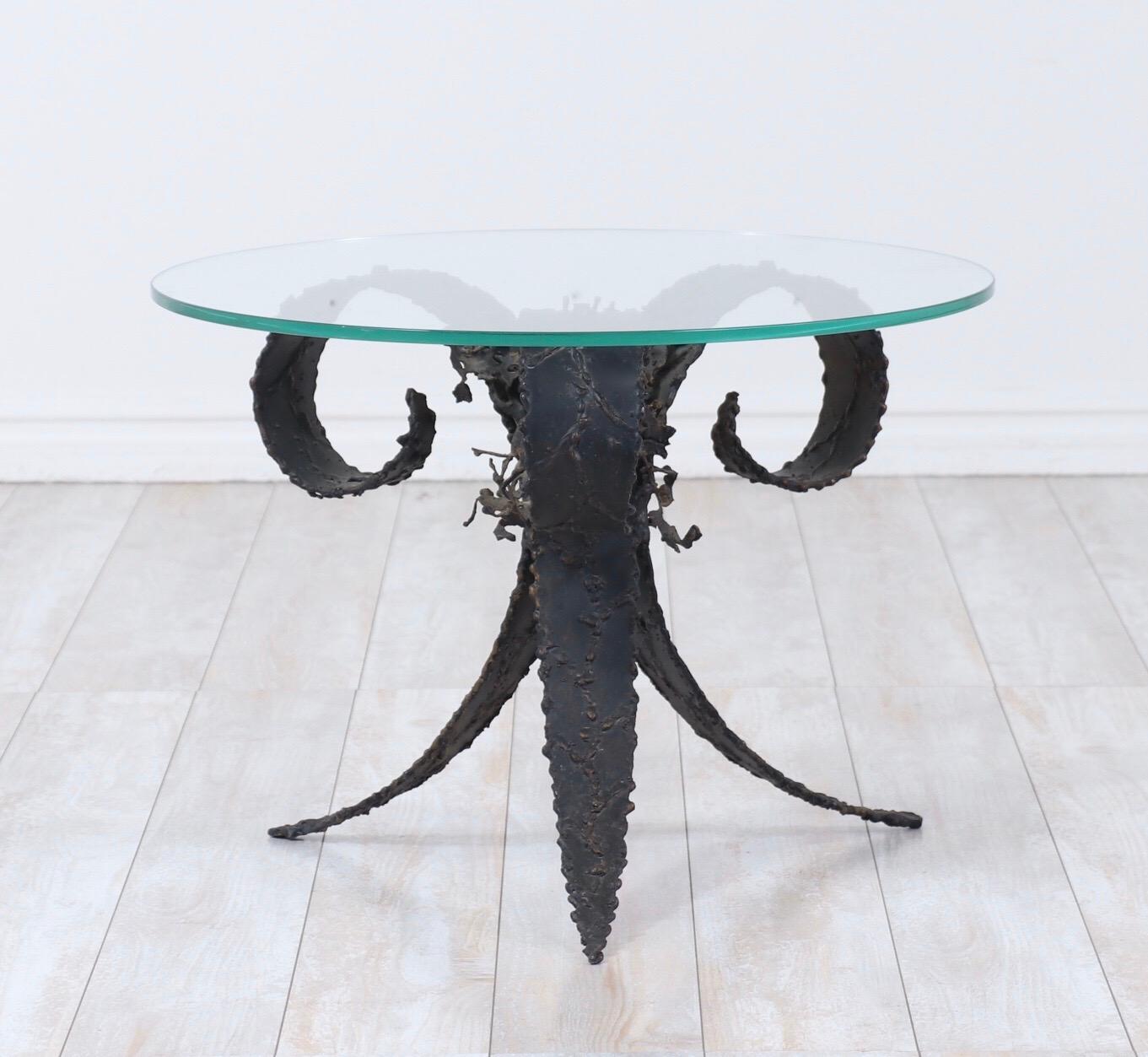 1960s small accent table with a round glass top by Silas Seandal.

This decorative table consists of a painted black torched steel base with floral accents in the Brutalist manner. 

Great table to add a bit of flair to modernist or contemporary