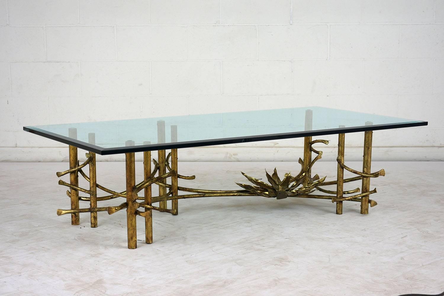 This 1960s Mid-Century Modern style coffee table features a whimsical brass base with a flower sculpture on top of overlapping branches. The branches are attached to the five pairs of table legs. The glass top is 3/4