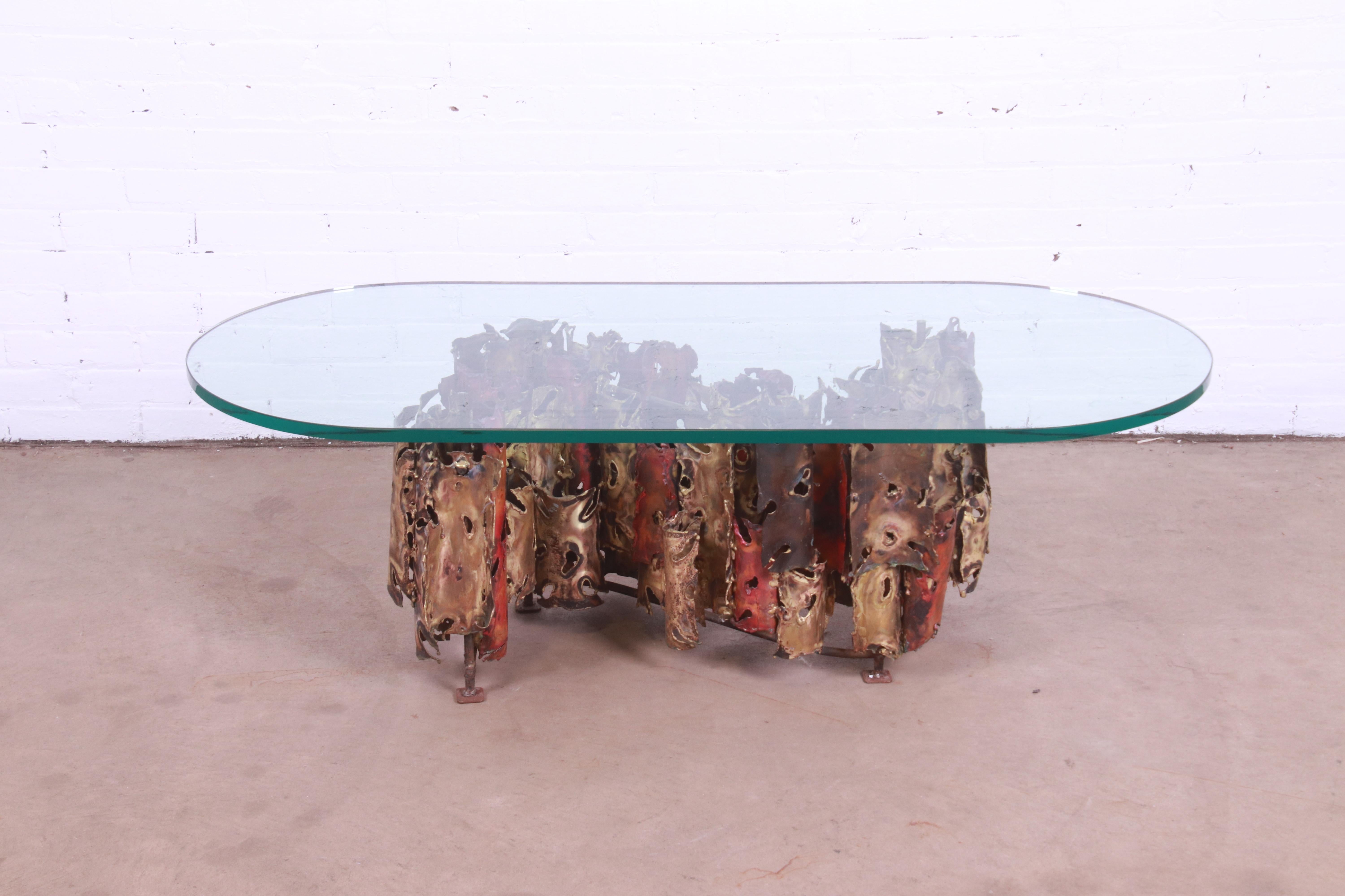 A stunning Mid-Century Modern brutalist coffee or cocktail table

By Silas Seandel

New York, USA, 1975

Mixed metal (brass, copper, bronze) sculpted base, with thick glass top.

Measures: 53.75