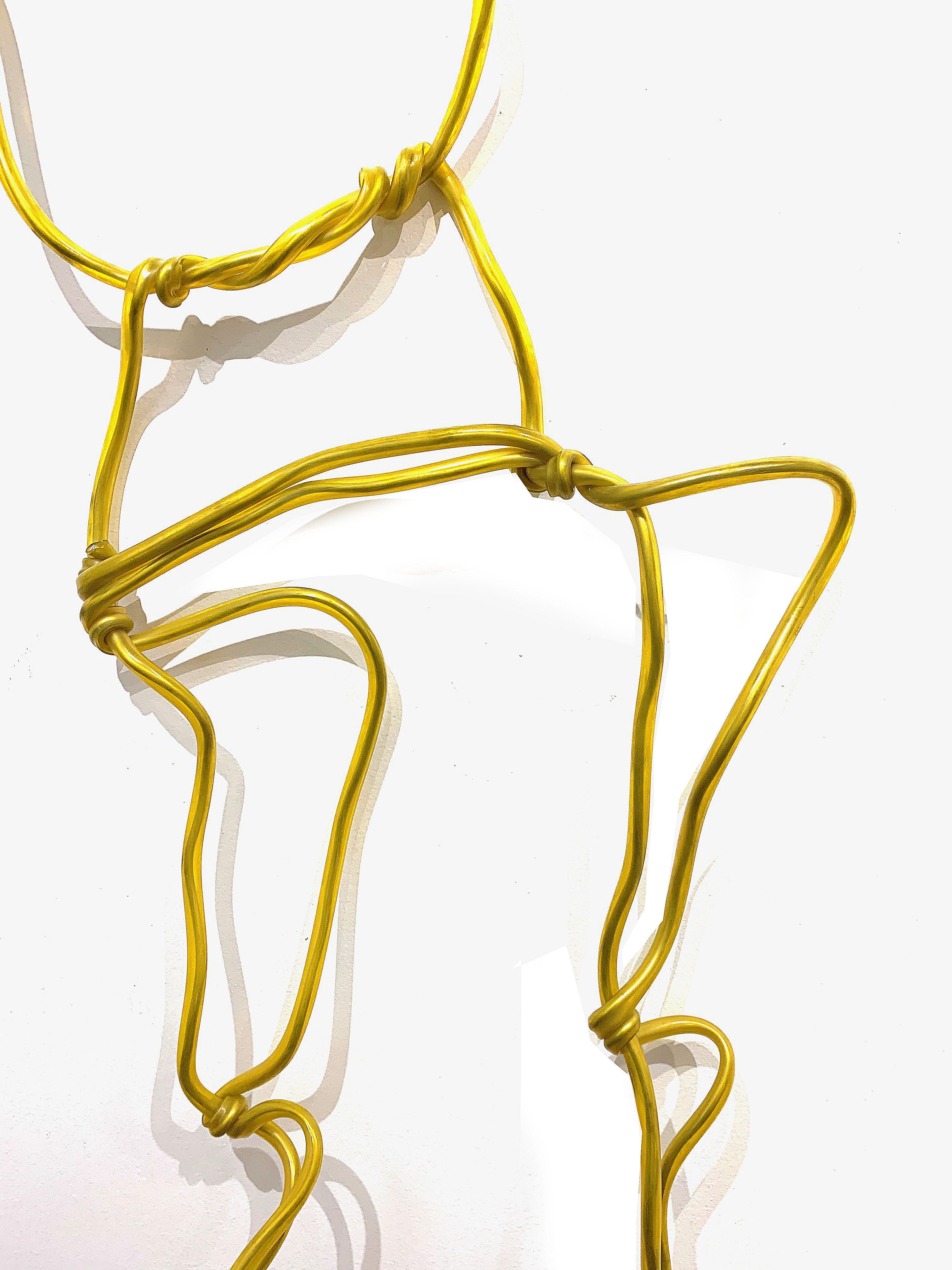Sculpture made of yellow plastic tubing and aluminum. This figurative piece can be placed in various poses, including displaying on a wall or in a hand stand. Dimensions given are approximate, as the overall height and width depends on how the