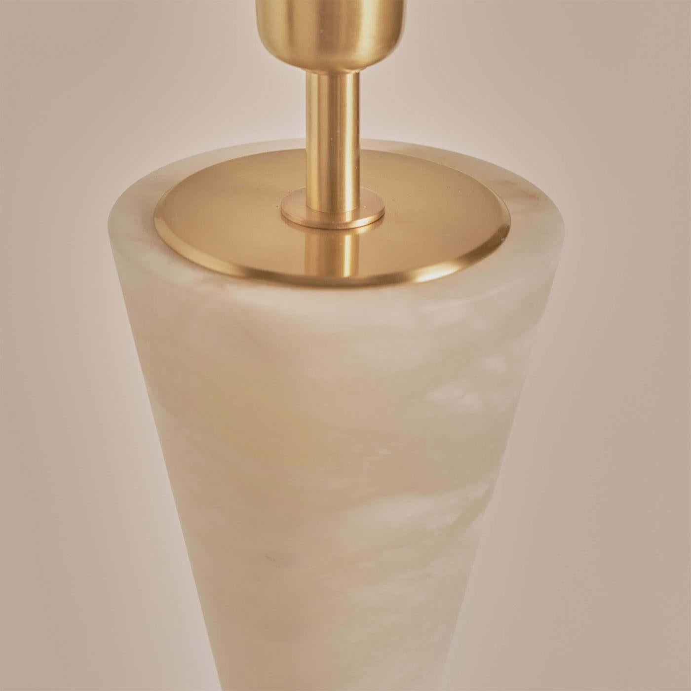 The Silhouette table lamp consists of two alabaster cones hoes vertices meet through a decorative solid brass sphere. Its curved shape gives the light an elegant and sophisticated profile combining the alabaster's heaviness with the brass's
