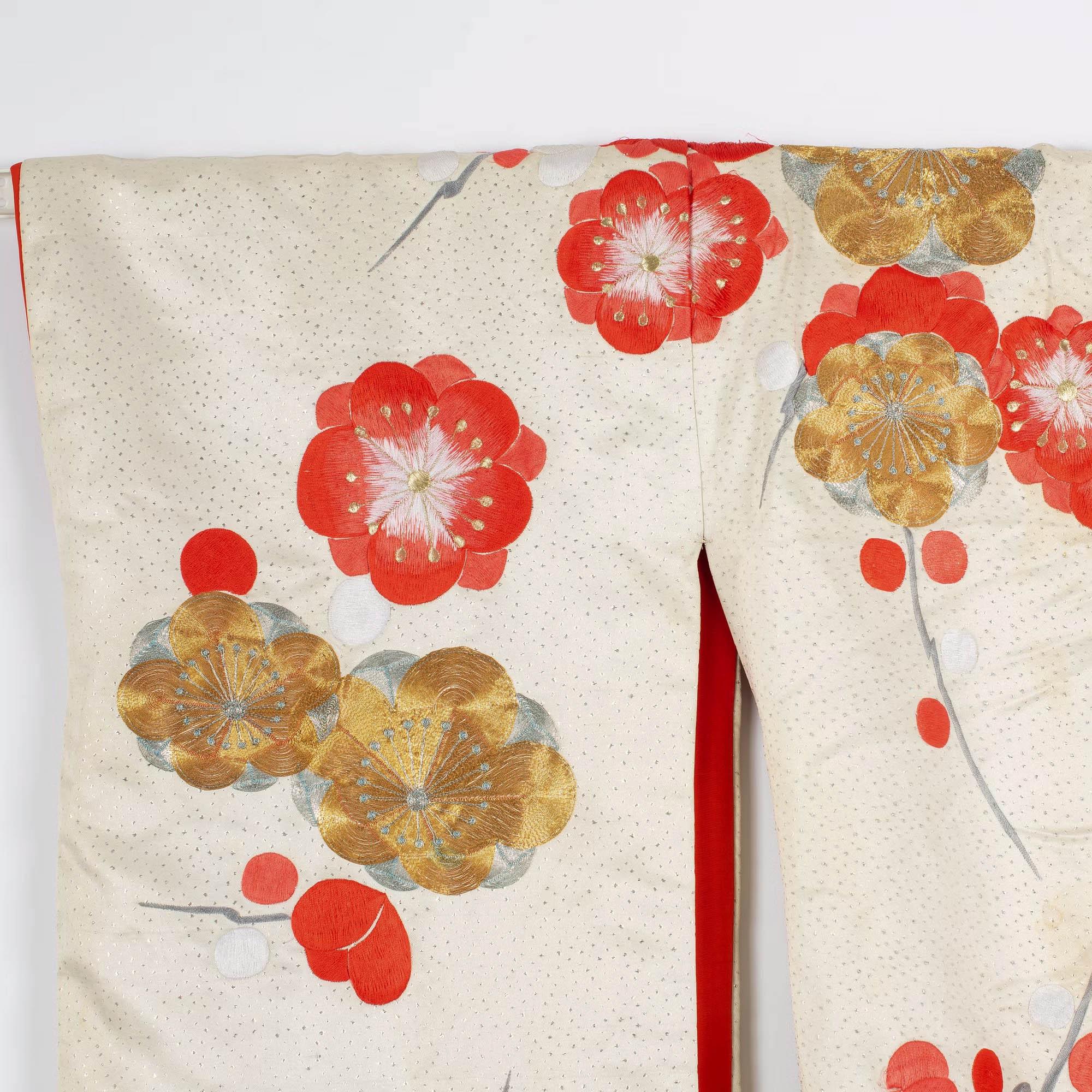 Kimono giapponese, riccamente decorato con ricami policromi con fili di seta e metallici, con un motivo di prunus in fiore su un fondo bianco crema. Foderato con seta rossa brillante.