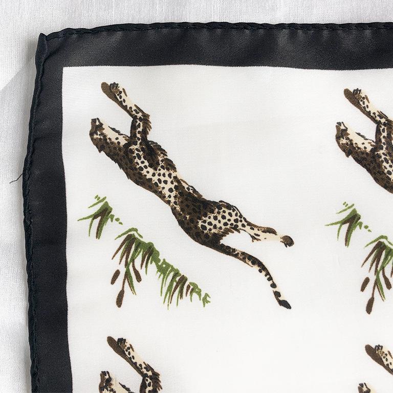 Beautiful cheetah print scarf. This piece has a white background and features cheetahs printed with a black frame around the edge of the scarf. This piece would be great as a neck tie or tied around a bag. Alternatively, it would also be great