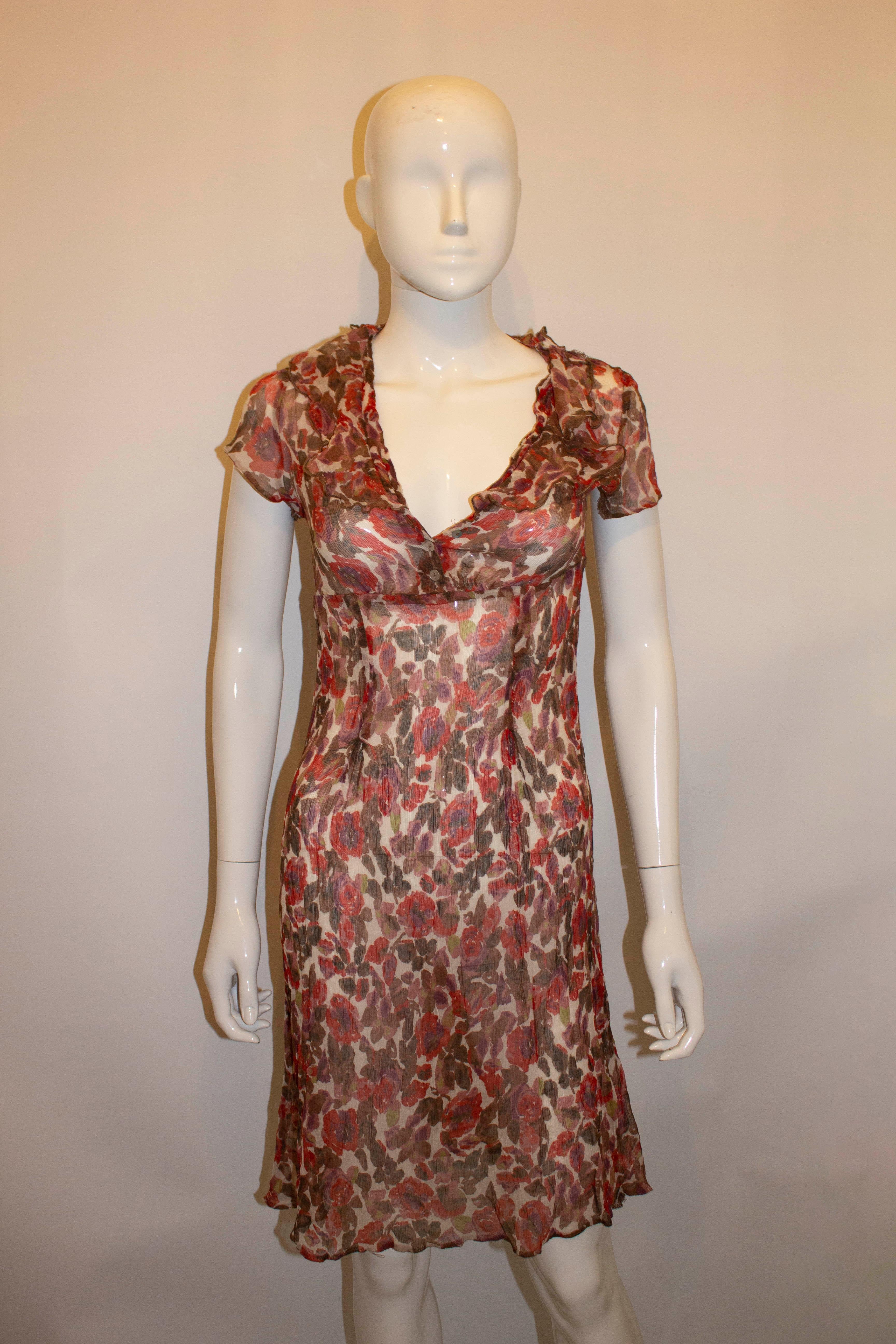A pretty silk chiffon tea dress with a button front and ruffles around the kneck. The dress has ca sleaves and a self fabric tie back. Measurements: Bust 35/6'', length 38''