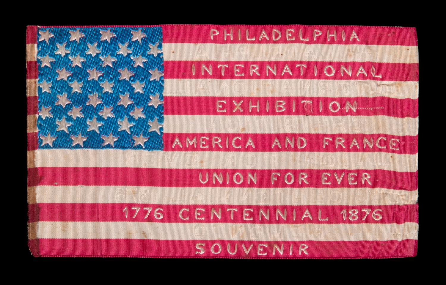 EXTRAORDINARY SILK FLAG MADE FOR THE 1876 CENTENNIAL INTERNATIONAL EXPOSITION IN PHILADELPHIA, WITH WOVEN TEXT ON EITHER SIDE, PROBABLY MADE AT ONE OF THE FRENCH EXHIBITS AT THE FAIR AND SOLD AS A SOUVENIR 

American national flag, made of silk, for