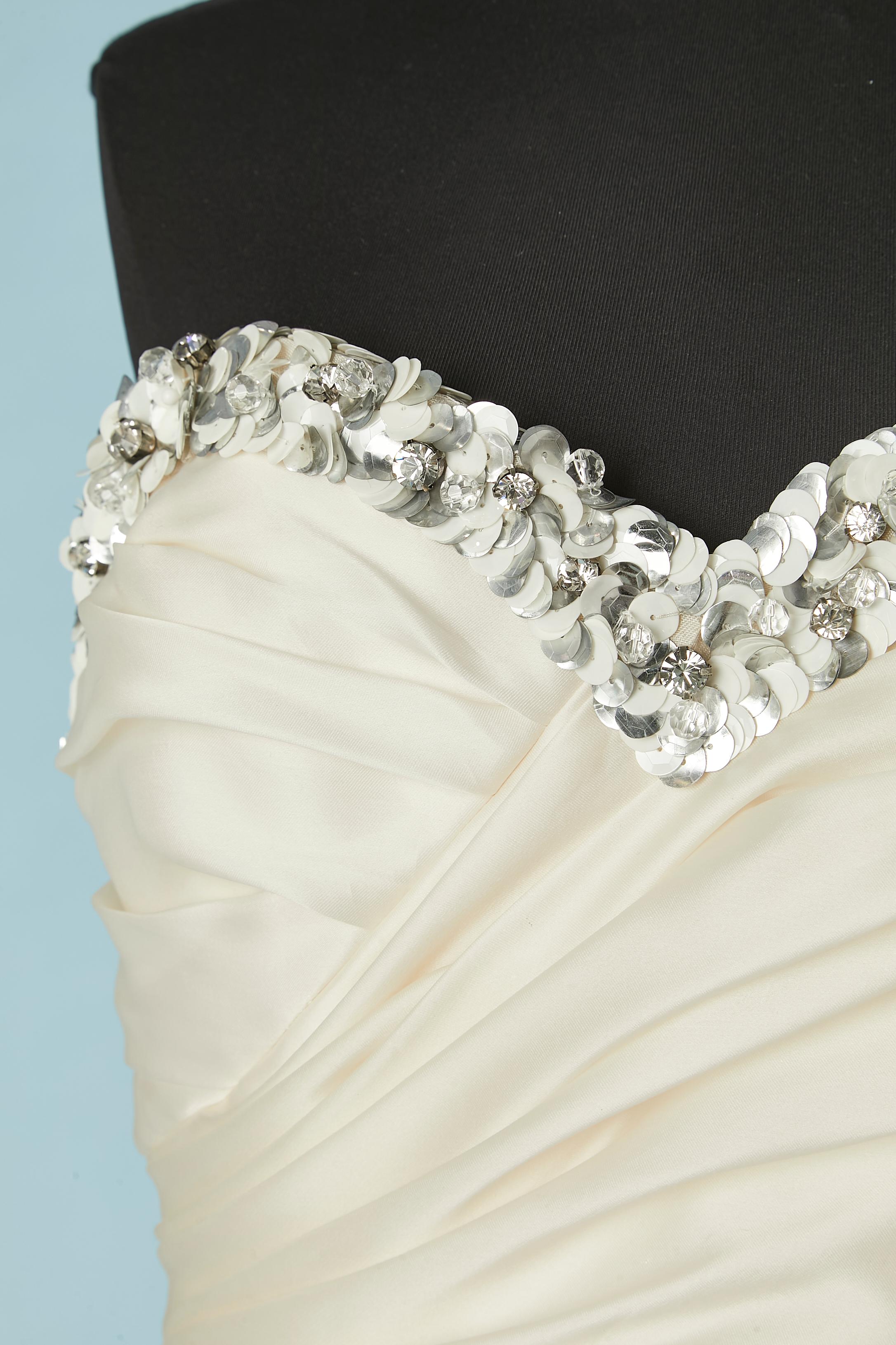 Robe de soirée en soie ivoire avec drapé,  des volants, des paillettes et des broderies en strass. Doublure en soie également. 
Bustier à l'intérieur avec fermeture à glissière et crochet sur le côté gauche. Deuxième fermeture à glissière sur la