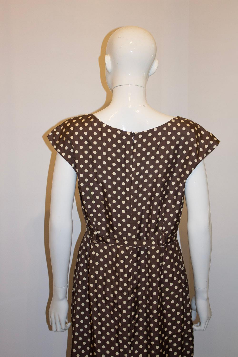A wonderful Summer silk dress by Marilyn Moore. 
With a brown ( the new black) background and cream spots, the dress has a round neckline with tuck detail and self fabric belt.It has a self  fabric belt and has a 10 1/2'' slit at the back.
Size UK