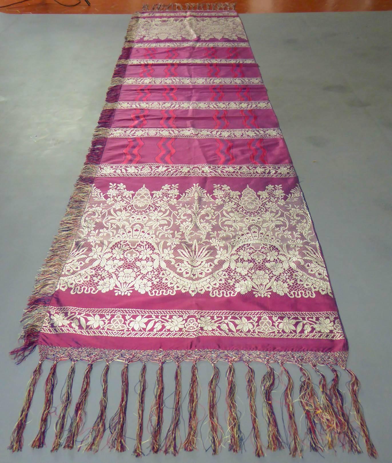 Circa 1860

France Lyon

A surprising woven stole with a lace decoration from an unidentified Lyonnais factory dating from the Second Empire. Silk lampas with silver plaited border and plum taffeta. Decor with ruffles of lace and ribbons of waving
