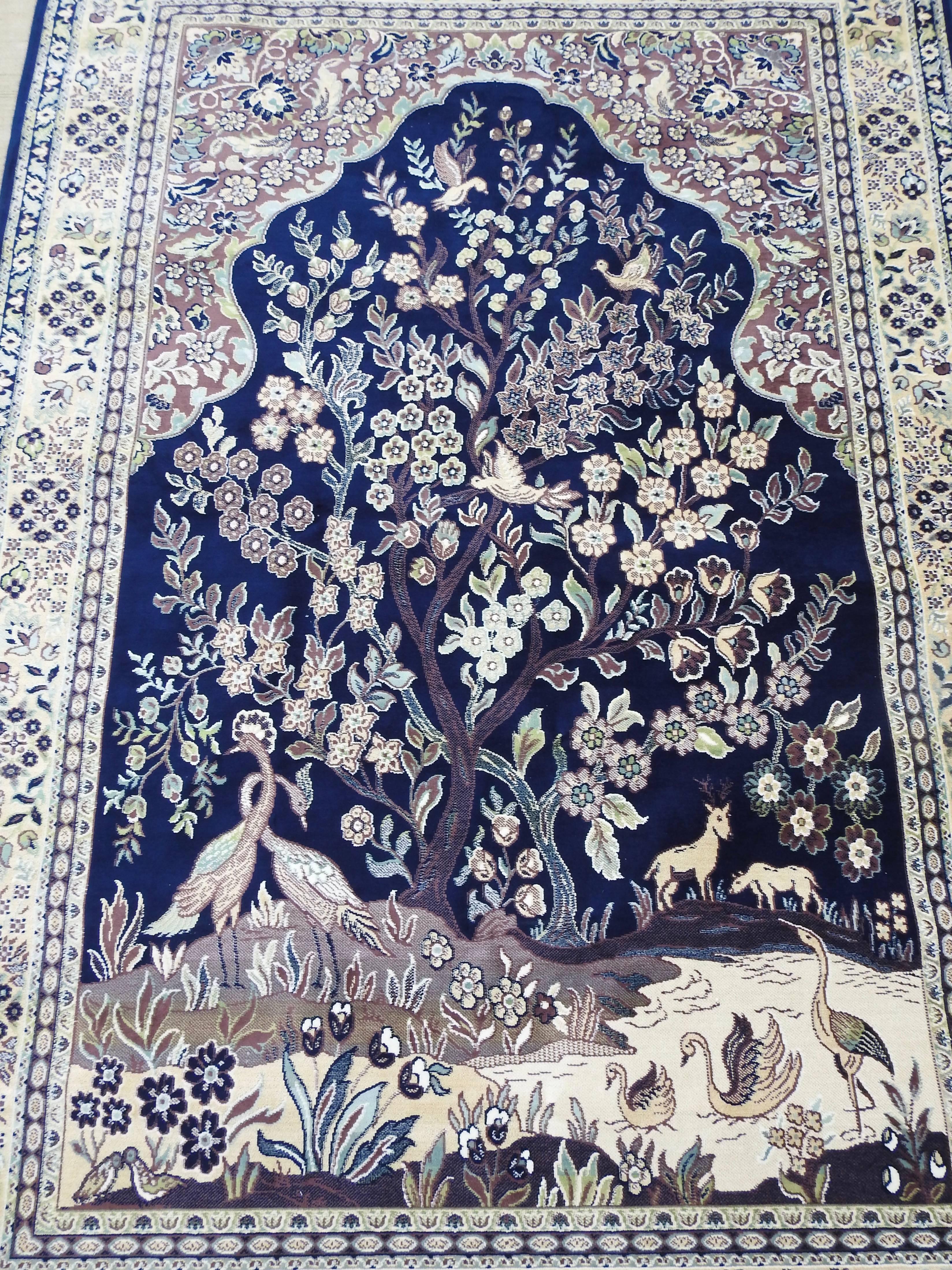 Soft shades of navy blue, lavender and cream make this rug a beautiful melody of silk. Flowers, trees and a variety of animals are surrounded by a decorative border. There is fringe on the ends to complete the look. A rod pocket has been added to