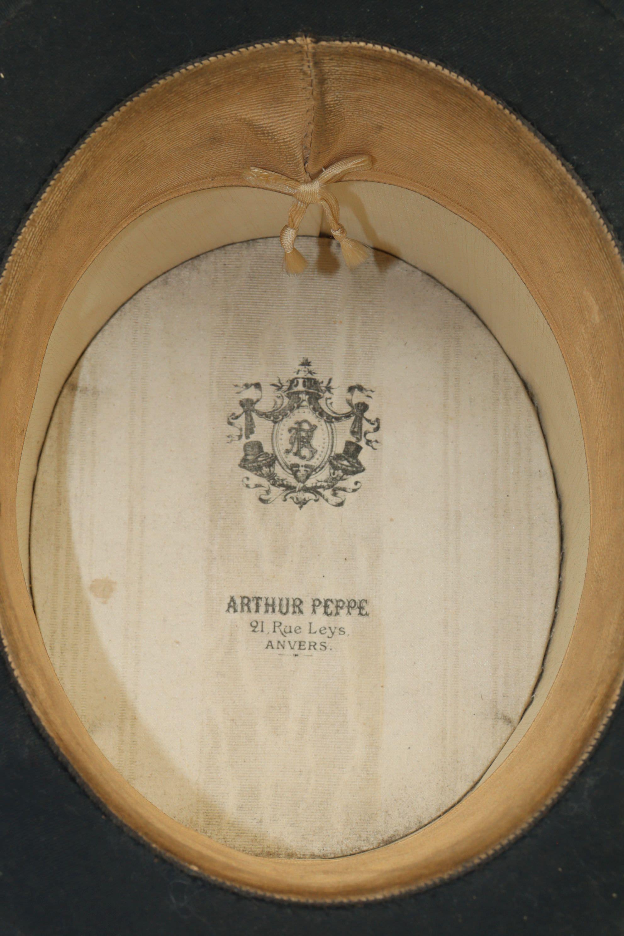 This silk top hat is housed in its original cardboard travelling case. It was made by Arthur Peppe of 23 Rue Leys in Anvers, which is the name given to Antwerp by French speakers. The makers mark on the inside of the hat is printed on watered silk