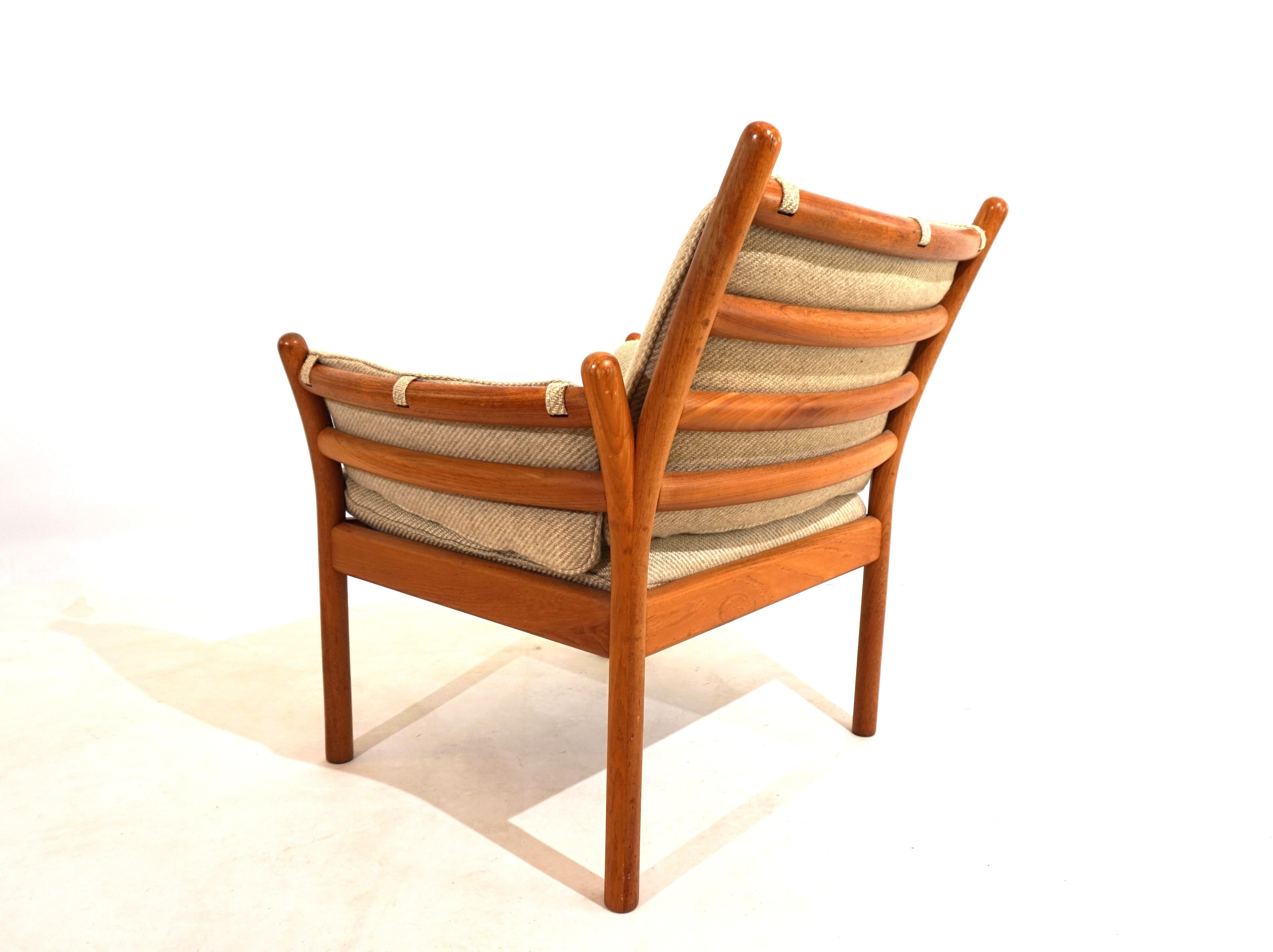 A Genius teak armchair in excellent condition from CFC Silkeborg. The attractive wooden frame with a very beautiful grain and a honey-colored color shows hardly any signs of wear. The covers, which are made from a beige brown wool fabric, are also