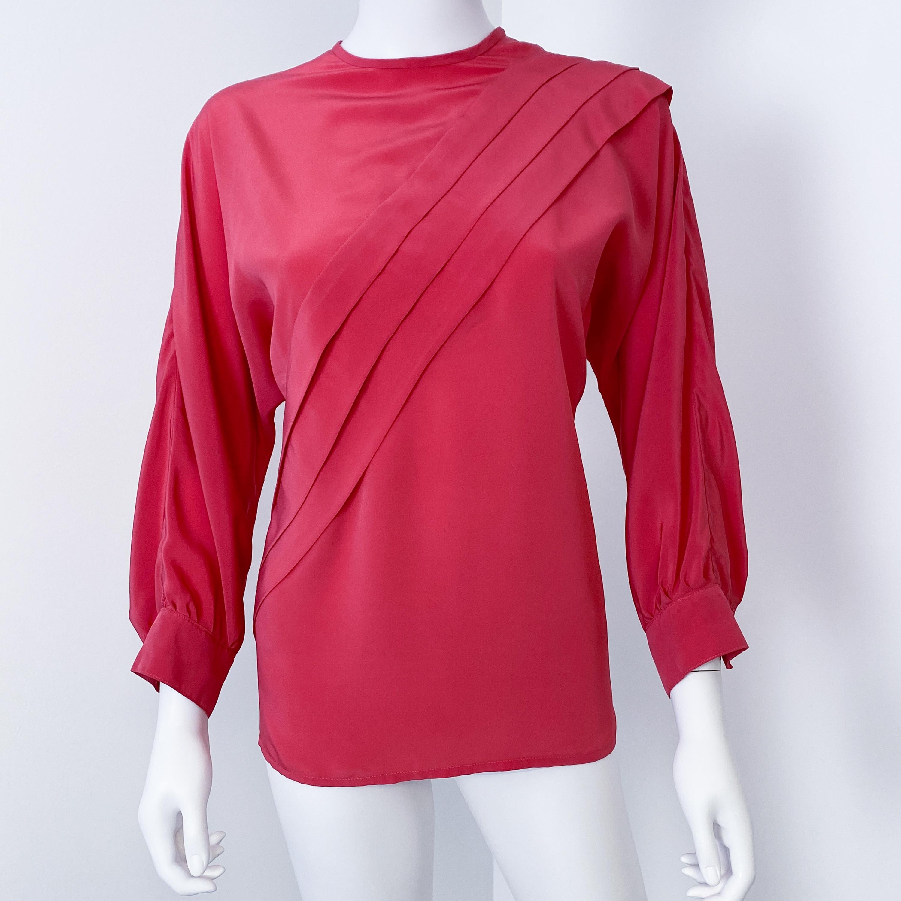 This vibrant 1980s blouse features a silky polyester-viscose blend in fuchsia pink, accented by geometric origami pleats. Button closures at the back and neckline add elegance, while 3/4-length sleeves with pleated button cuffs create graceful