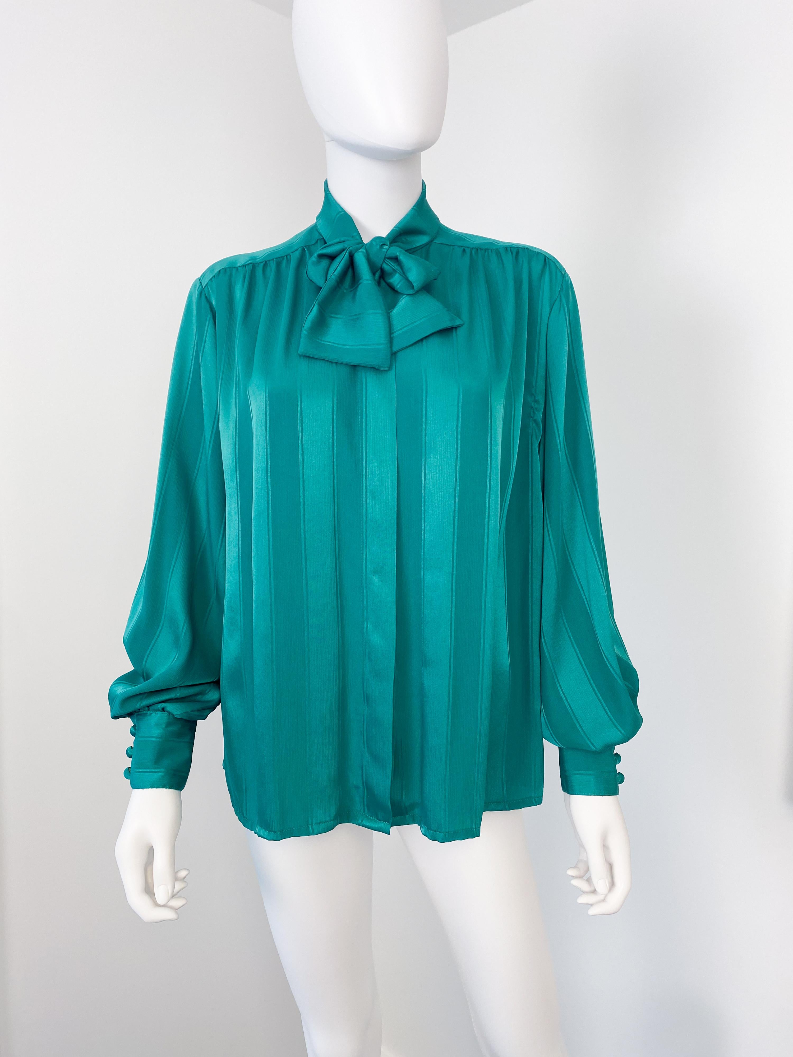 This stunning vintage 1980s blouse, crafted from silky polyester, features an elegant attached scarf-bow for a sophisticated touch. Its vibrant emerald green fabric is enhanced by a tone-on-tone geometric striped pattern, adding depth and