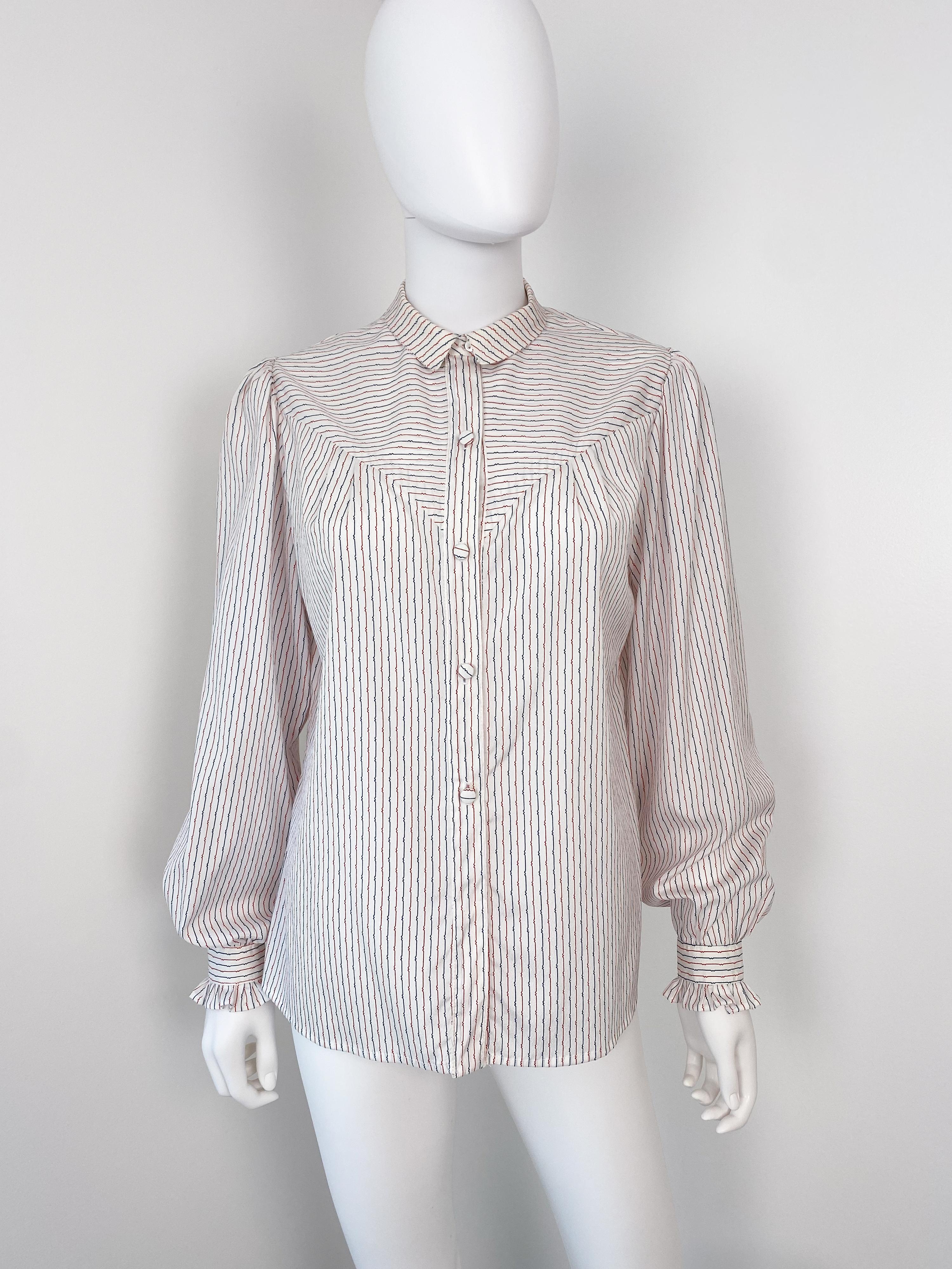 This charming vintage 1980s western-style blouse is crafted from silky viscose-polyester, offering both elegance and nostalgic flair. The crisp white fabric is adorned with striking red and blue stripes, creating a bold yet timeless look. A