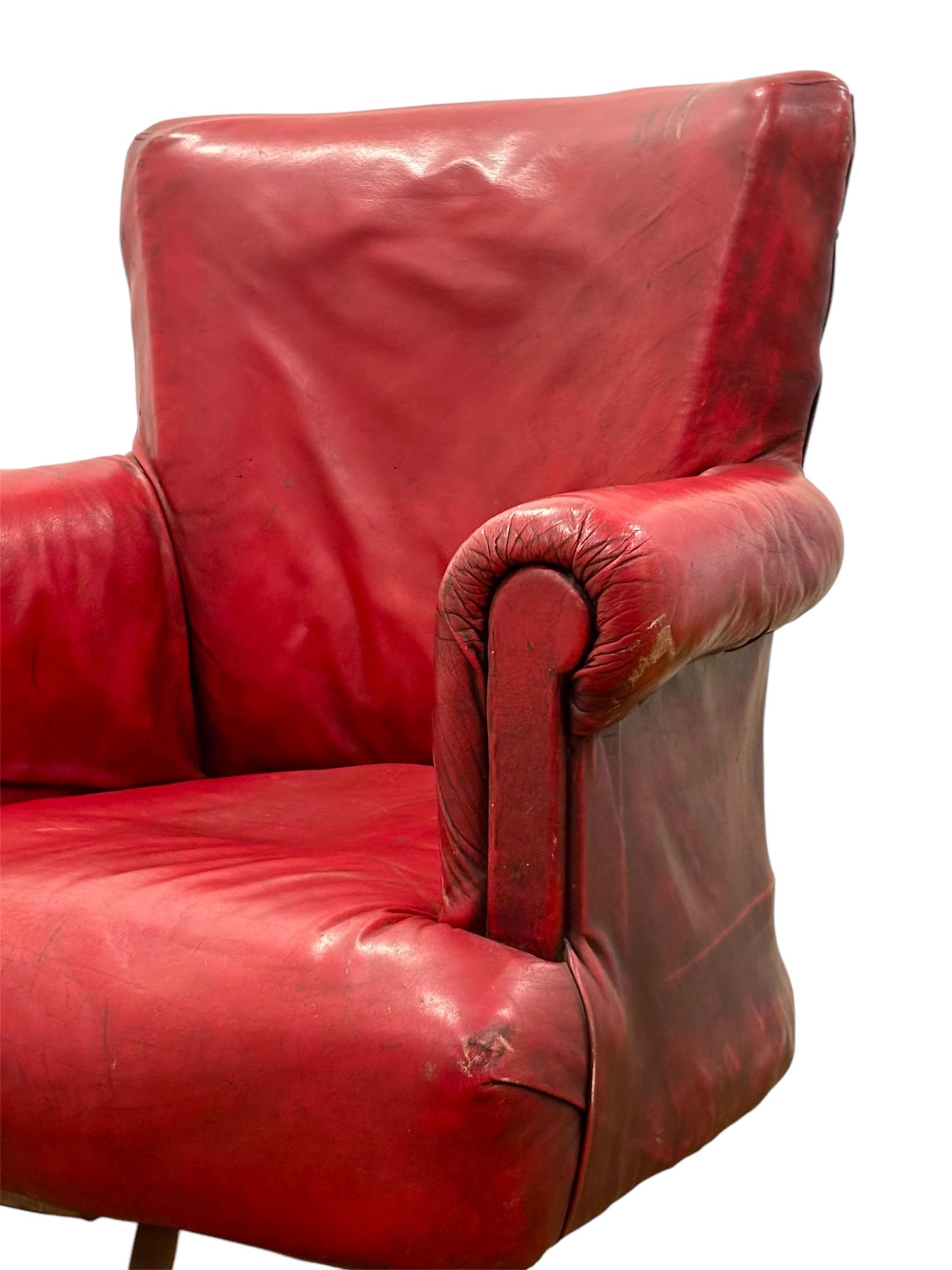 Sillón Club inglés giratorio CIRCA 1.900, realizzato in pelle di colore rojo marroquí, con patas de madera de roble e ruedas de latón. 
