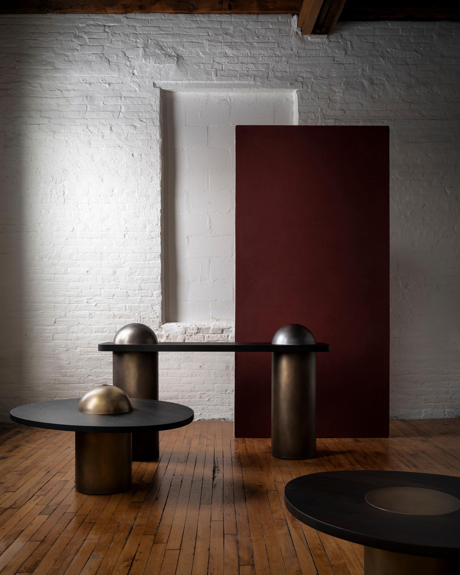 Inspired by the form and function of grain silos, the sculptural Silo Console Table features solid wood and hand-finished brass or stainless steel wrapped legs.

This listing includes two removable brass domes that sit atop the table. The hollow