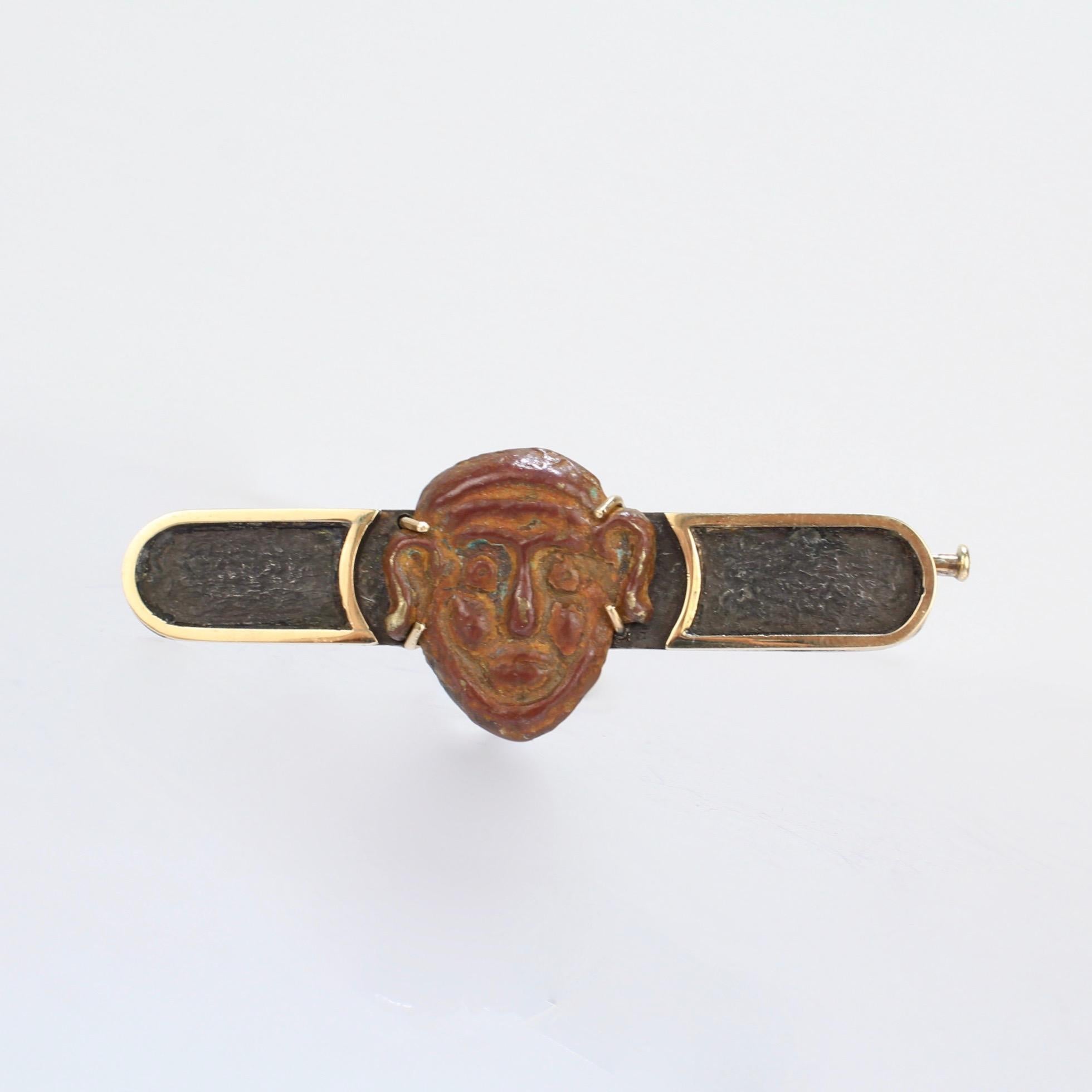 A wonderful bar pin by Paul Haig, the long-established and well-renowned custom jeweler and Asian dealer from Rochester, Michigan.

Comprised of a small bronze Japanese mask (probably from a Noh play) set on a liver sulfured silver bar pin with 14K