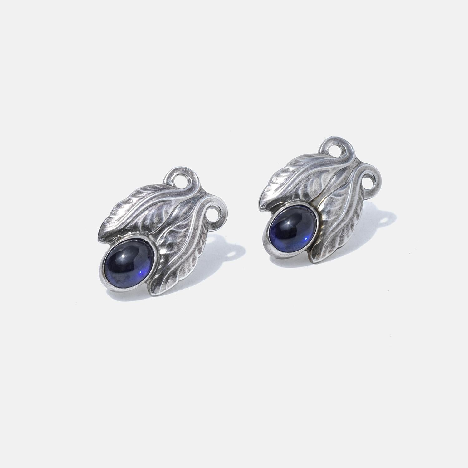 These sterling silver earrings feature deep blue stones nestled within leaf-like designs, adding a touch of nature-inspired elegance. The intricate leaf patterns cradle the stones, reflecting a vintage aesthetic. The earrings are designed with screw