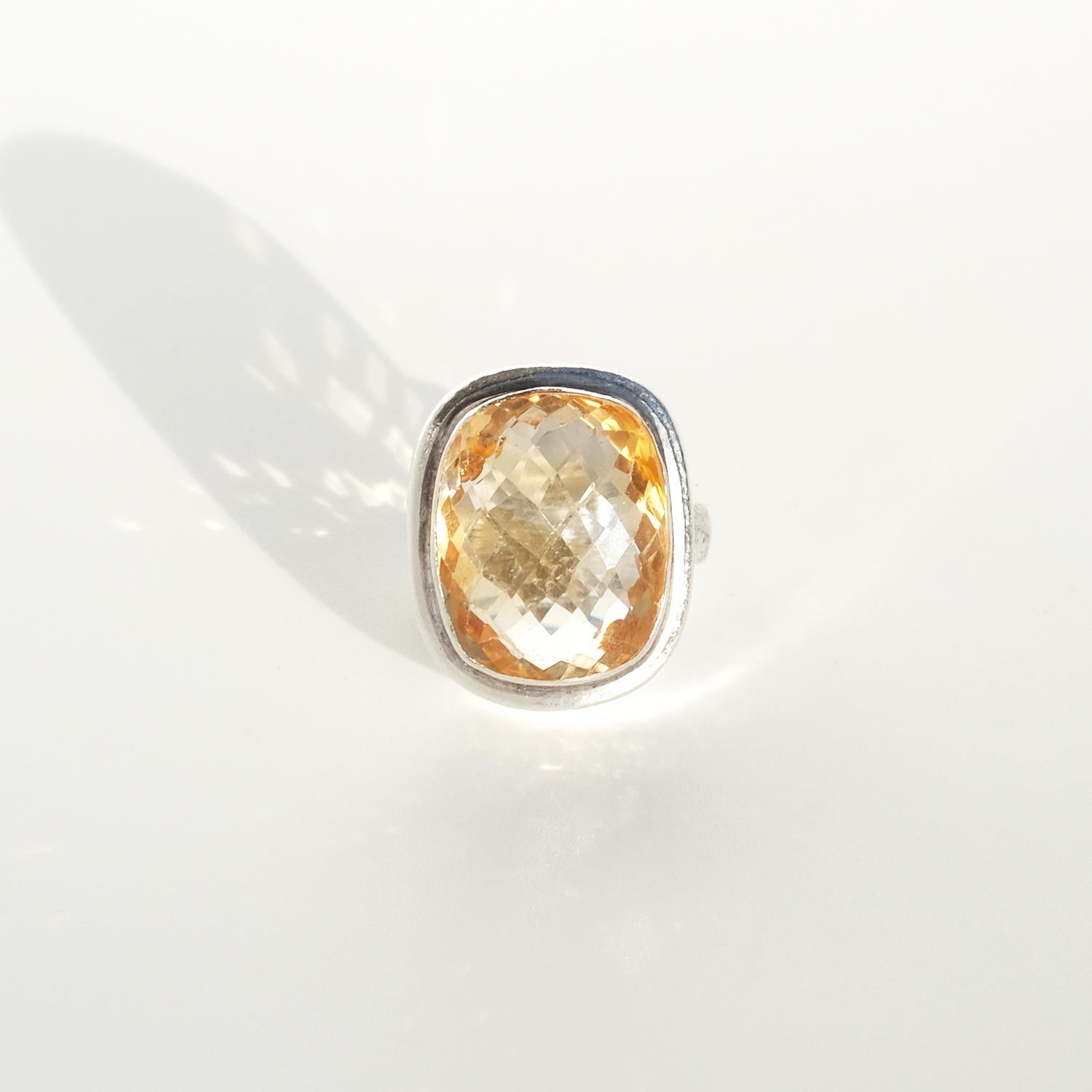 This striking silver ring showcases a large, rectangular-cut citrine with numerous facets that catch the light beautifully. The citrine's warm golden hue adds a vibrant contrast to the rustic, handcrafted silver band. Set in a bold and prominent