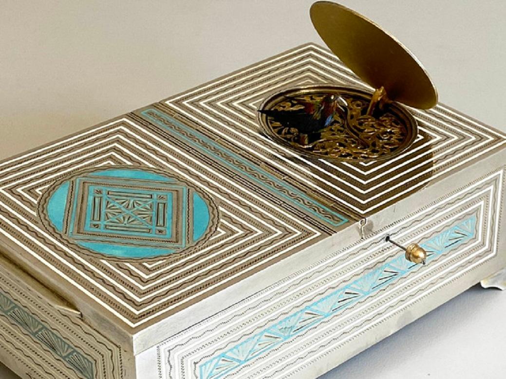 Eine seltene und exquisite Art Deco Zigaretten- und Vogelspieldose aus Silber und Emaille. 
der Singvogel mit schönem, mehrfarbigem Gefieder mit roten, gelben und blauen Akzenten, Schnabel, Schwanzfeder, Flügelschlag und Drehung im Takt des