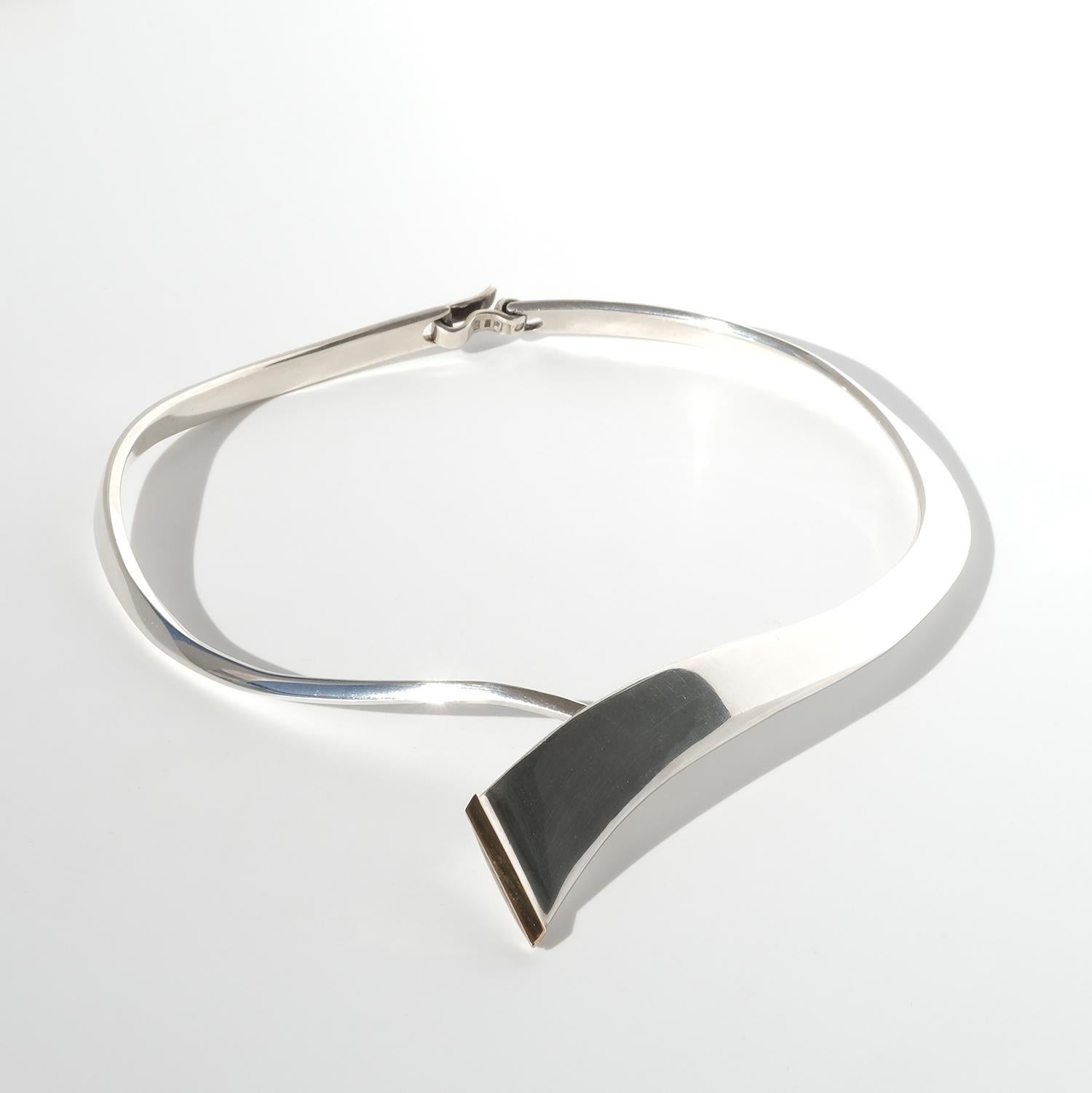 Questo anello da collo in argento e argento dorato presenta un design audace e scultoreo con una forma dinamica e asimmetrica che si curva elegantemente intorno al collo e si appoggia fluidamente sulla clavicola. La sezione frontale ampia e piatta