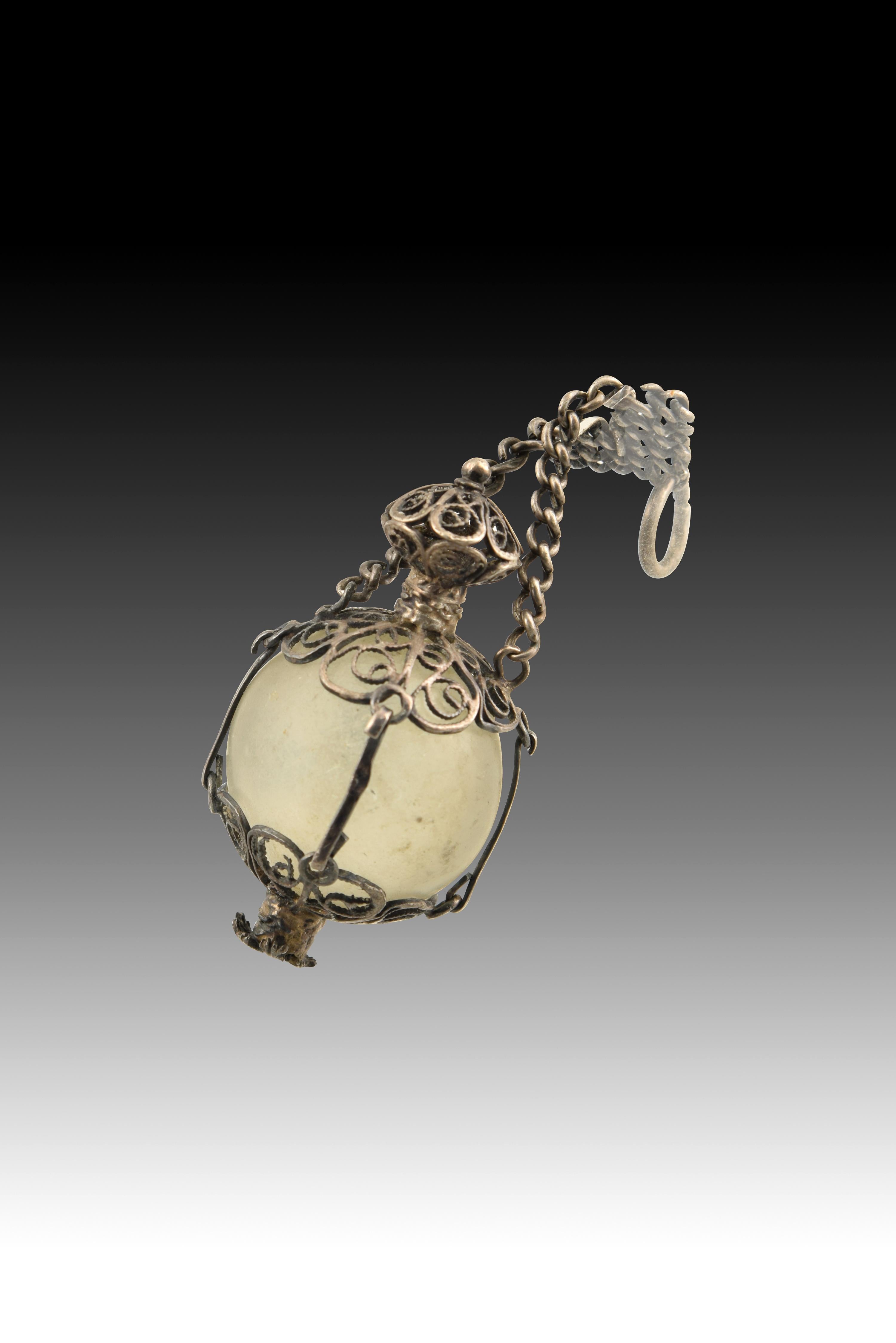 Pendant. glass, silver Century XVIII.
 A translucent white glass bead has been placed inside a frame of silver in its color made up of two areas worked in fretwork or filigree, a technique also present in the spherical shape that finishes off this