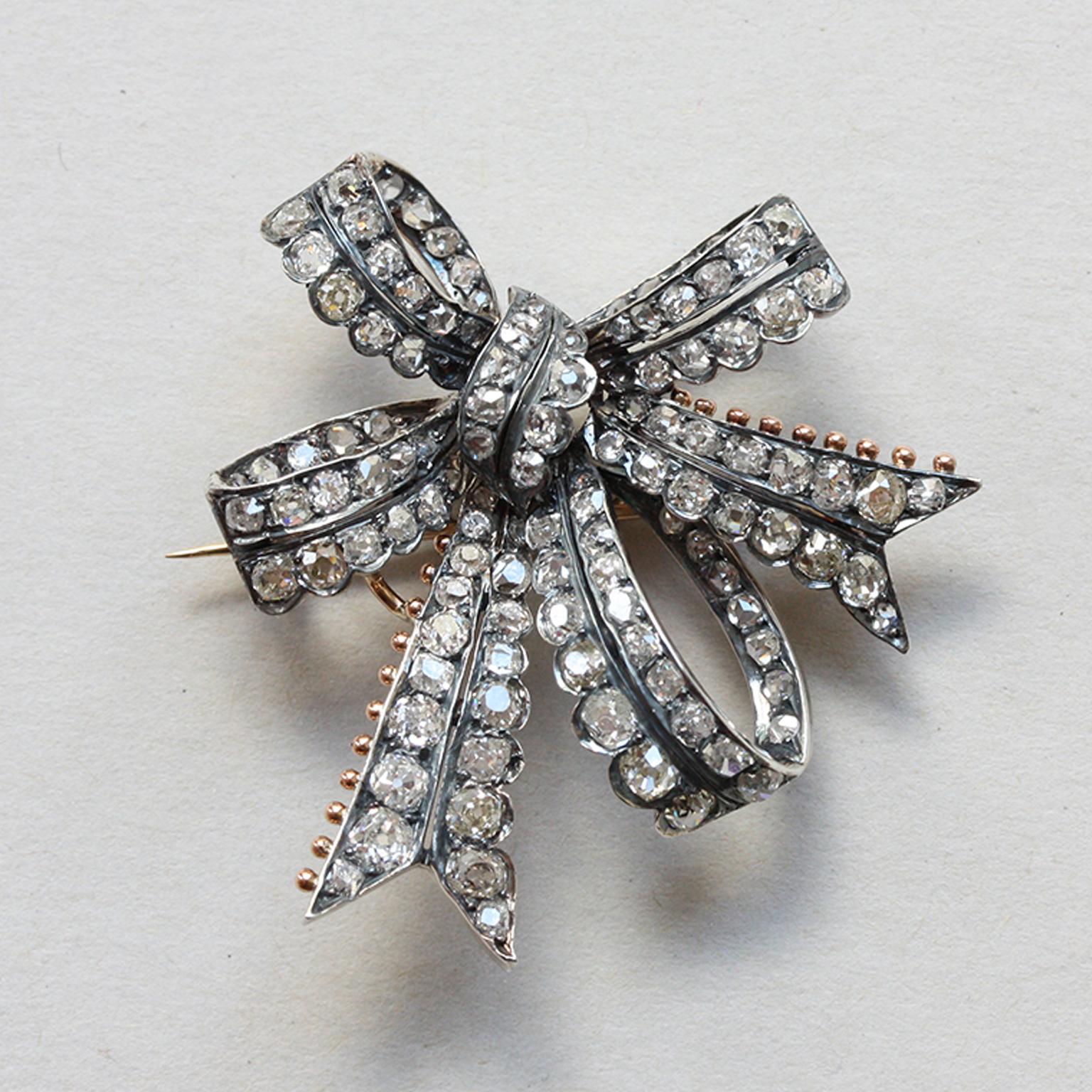 A silver double bow brooch set with chunky old-cut diamonds (app. 3.4 carats) with gold backing. One edge of the bow has scalloped sides and the ends of the ribbon are decorated with small gold balls. England, circa 1880.

weight: 9.92