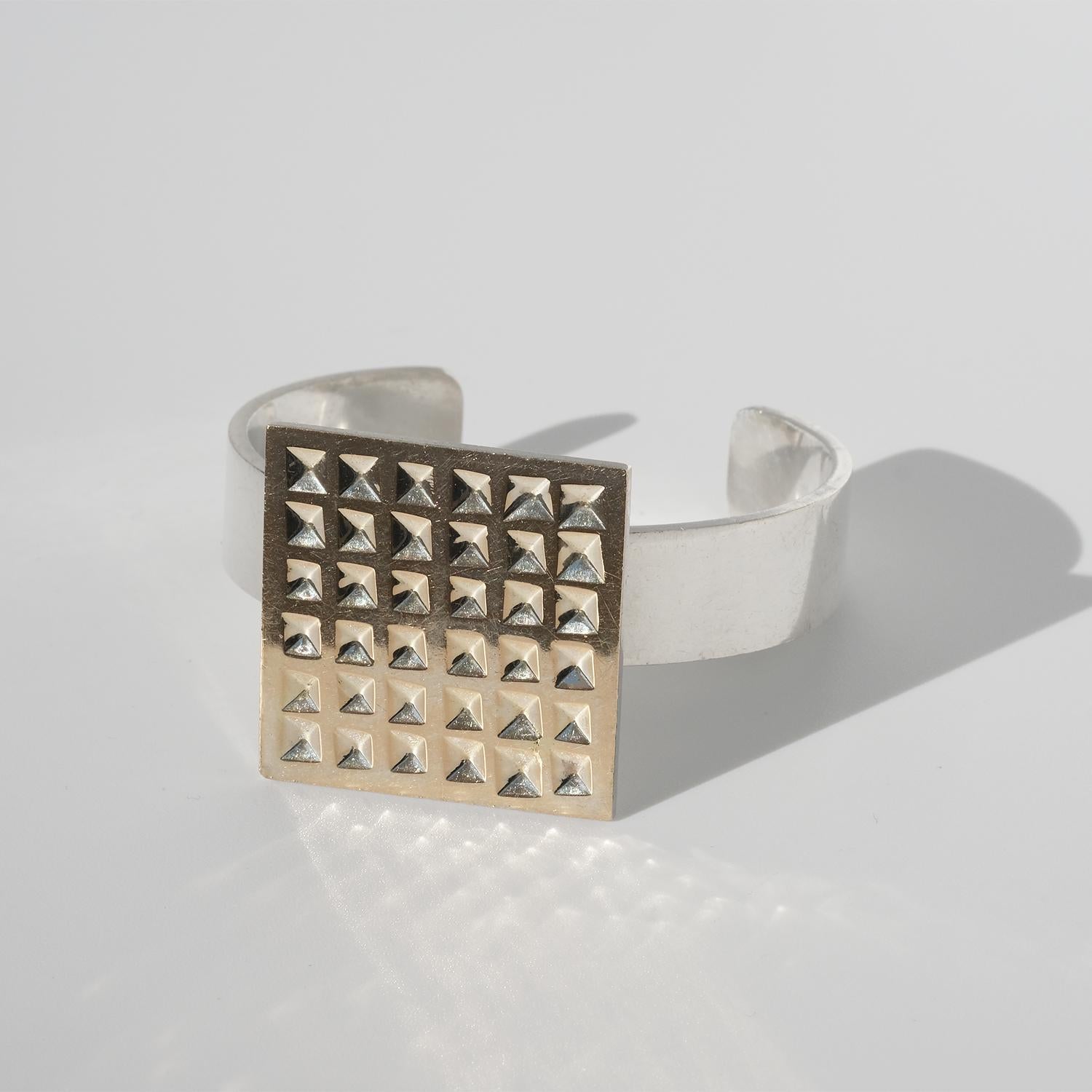 This sterling silver cuff bracelet has gold on its upper part. The fixed cuff bracelet is excellent with its firm, waffled adornment and geometrically curved arms. This bracelet is fun and elegant at the same time. It will give its wearer