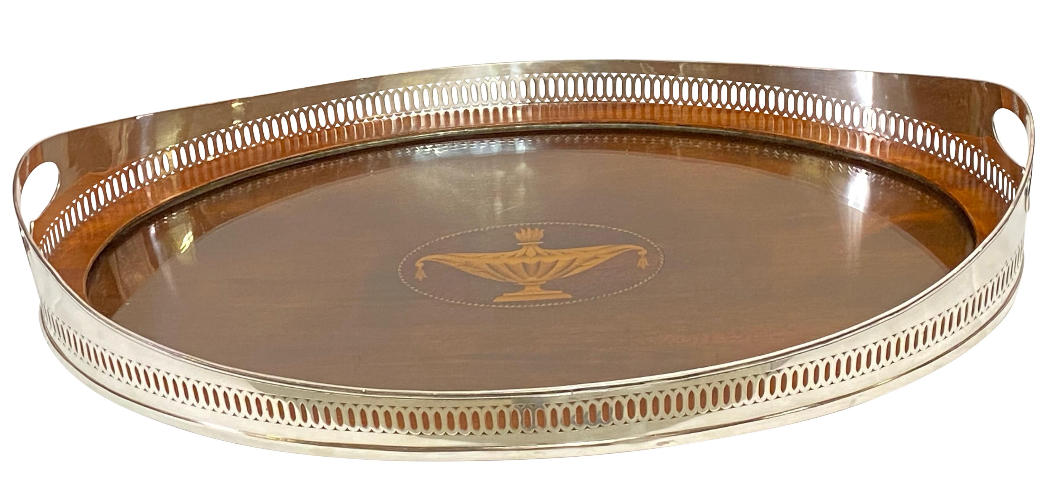 A Sheraton style silver on copper gallery serving tray with glass insert over mahogany center, and having a satinwood inlay center urn decoration.
England, early 20th century. 
Excellent antique condition.