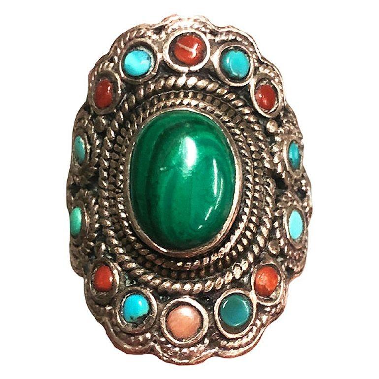 Questo anello con ciondolo in argento è impreziosito da un'incantevole gemma di malachite. Intorno alla bellezza centrale ci sono piccole gemme di turchese e diaspro che creano un intricato disegno ispirato alla natura. Questo squisito pezzo fonde
