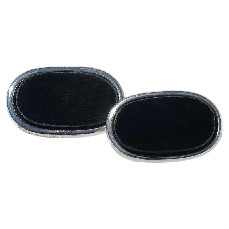 Ces boutons de manchette sont fabriqués en argent sterling et sertis d'obsidienne noire polie. La face avant est ornée d'une pierre rectangulaire légèrement surélevée aux bords arrondis, encadrée par une étroite lunette en argent. La surface noire