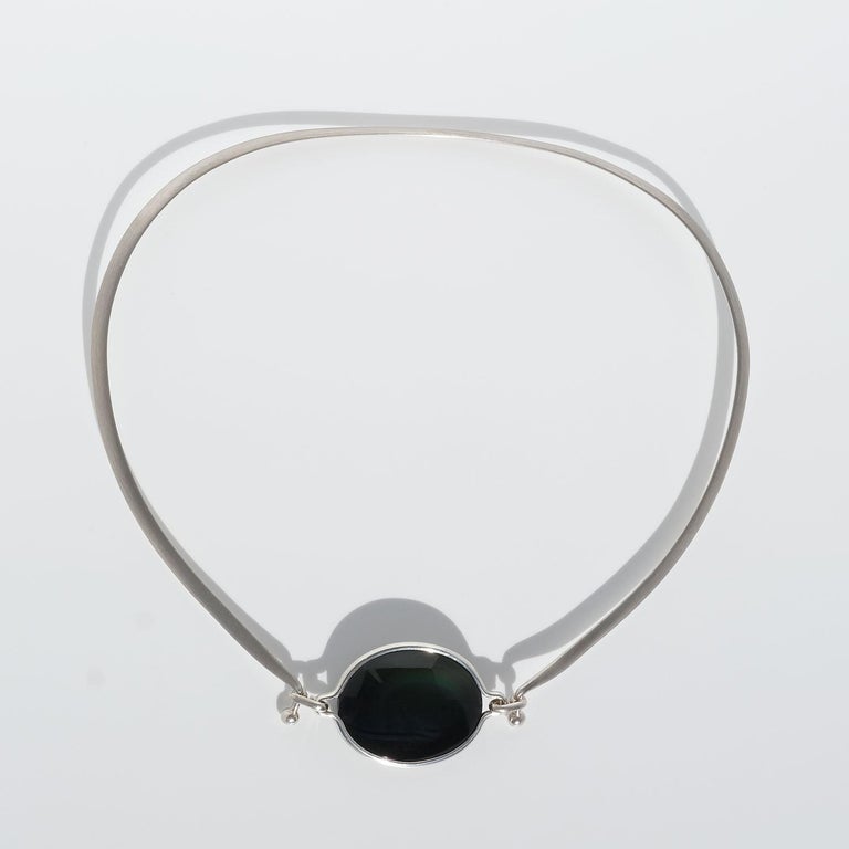 This sterling silver neck ring is adorned with an oval, glossy rainbow obsidian. The obsidian stone is attached to the necklace with two hooks and it is removable. In the rainbow obsidian, microscopic bubbles have formed which give rise to a rainbow