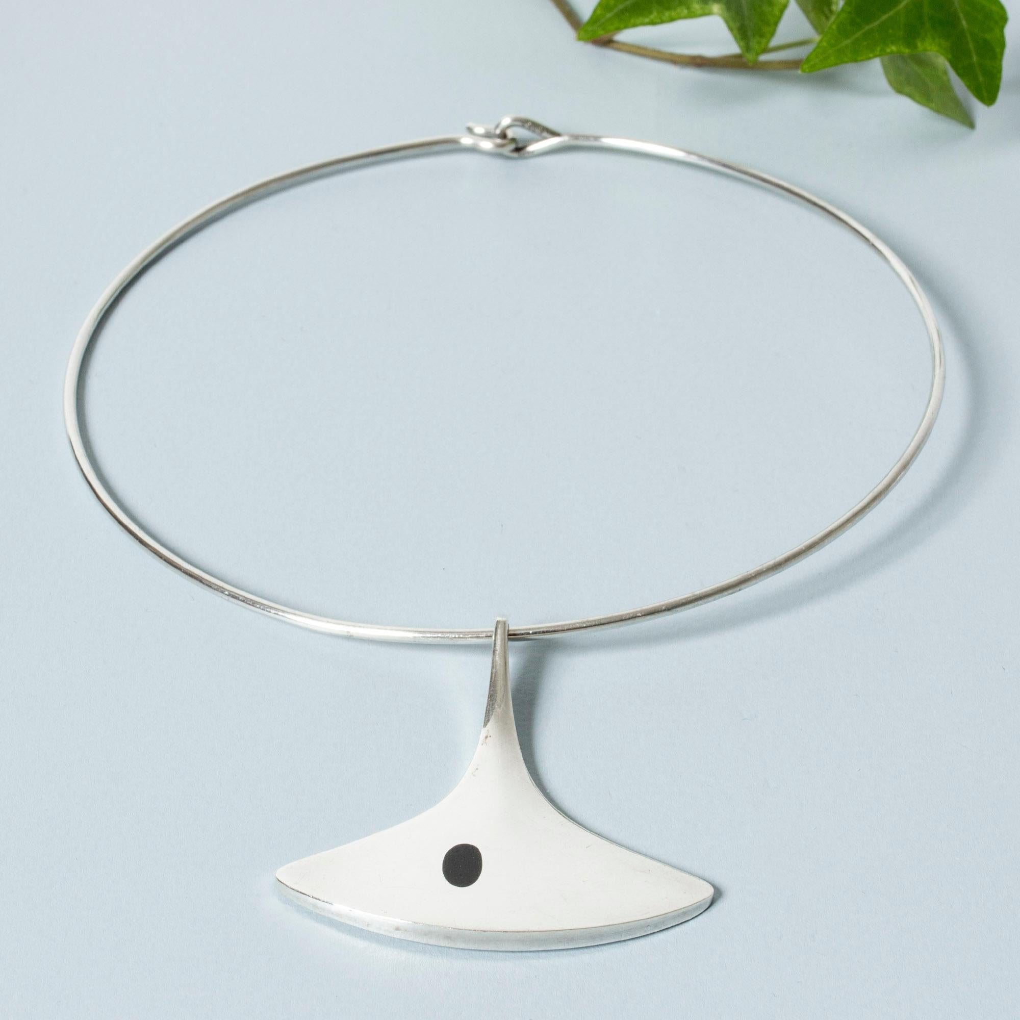 Striking silver neckring by Bent Gabrielsen Pedersen, with a pendant in a smooth, organic form. Onyx stone fleck. Appealing, streamlined look with a solid weight.

Height of pendant 5 cm, width 4.9 cm.