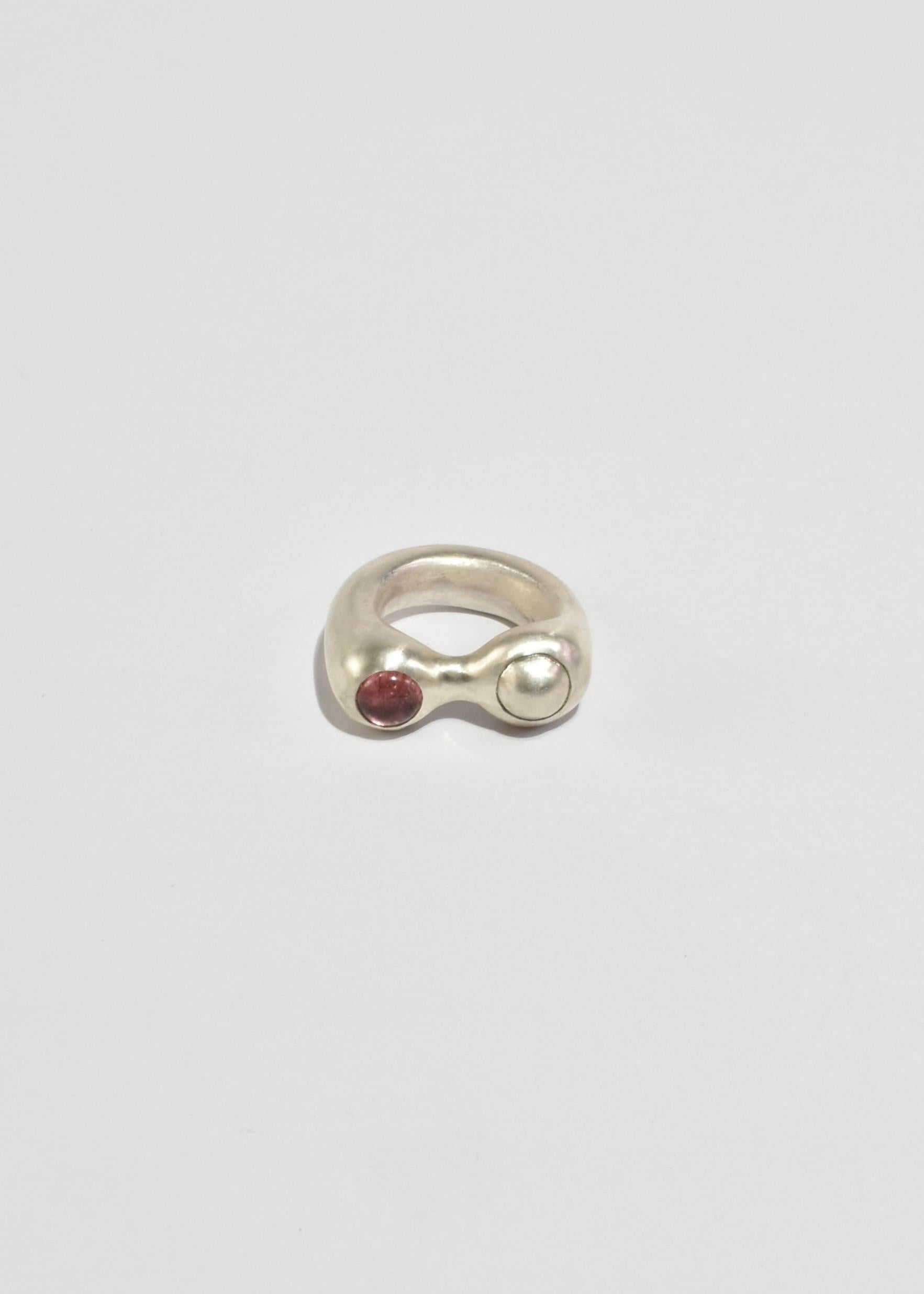 Sterling hand carved and cast organic shaped ring with a round pink tourmaline stones and a round silver cabochon.

Each piece is hand carved and finished in Virginia by Shauna Dunn of First Edition.

Material: Sterling silver, tourmaline.

We