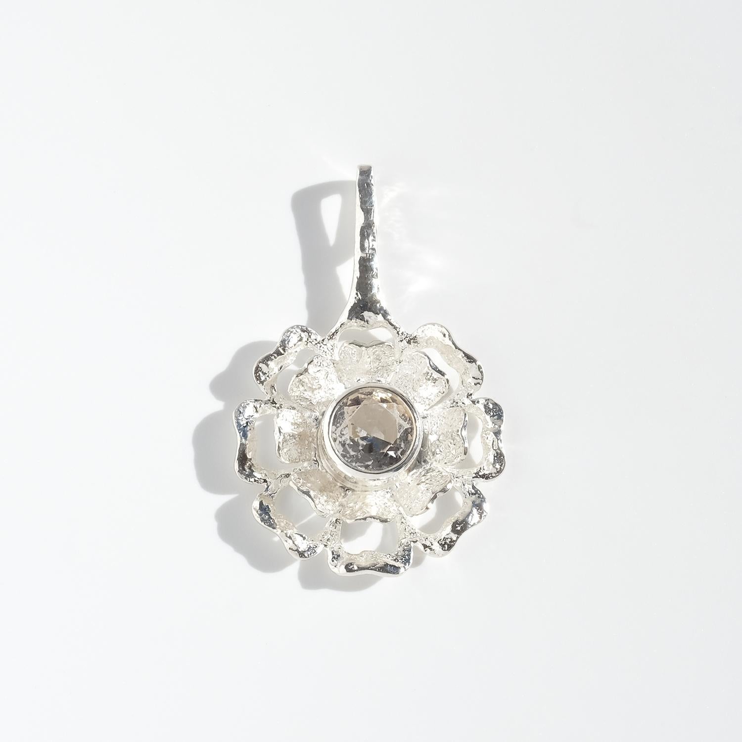 Questo grande ciondolo vintage è realizzato in argento con un grande cristallo di rocca al centro. Disegnato a forma di fiore stilizzato che ricorda una rosa selvatica, il pezzo presenta petali stratificati che si alzano leggermente per incorniciare