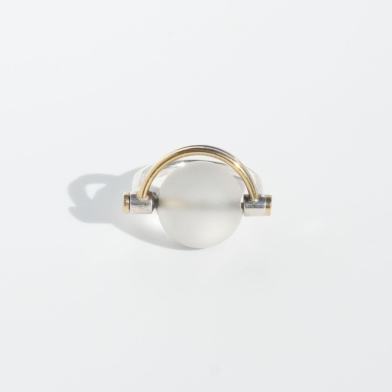 This silver ring is adorned with a frosted rock crystal ball which is surrounded by two parallel semi-circles, one in silver and the other in gilt silver. The semi-circles have prominent mounts and the u-shaped shank is rounded in itself.

Like the