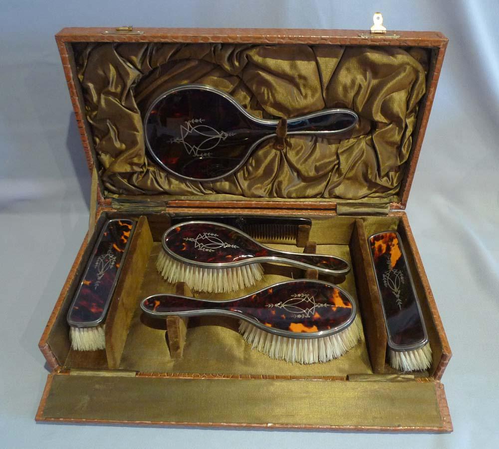 A very attractive George V un-used 6 piece brush and mirror set in silver and tortoiseshell with fine silver pique work to the back of each piece. Hallmarked for Hassett and Harper Birmingham, England 1924. All enclosed in lined case.