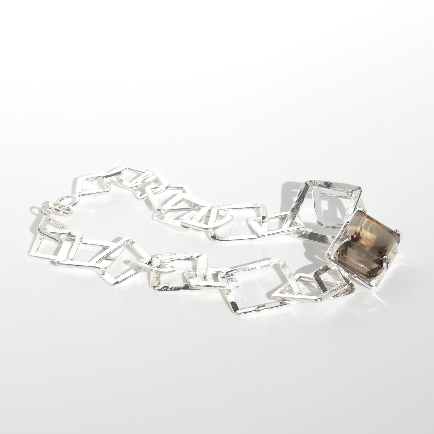 Questa collana in argento presenta una serie di maglie quadrate aperte, angolari e interconnesse che creano un design geometrico e scultoreo. Al centro è appeso un audace quarzo fumé rettangolare incastonato in una robusta cornice d'argento, che