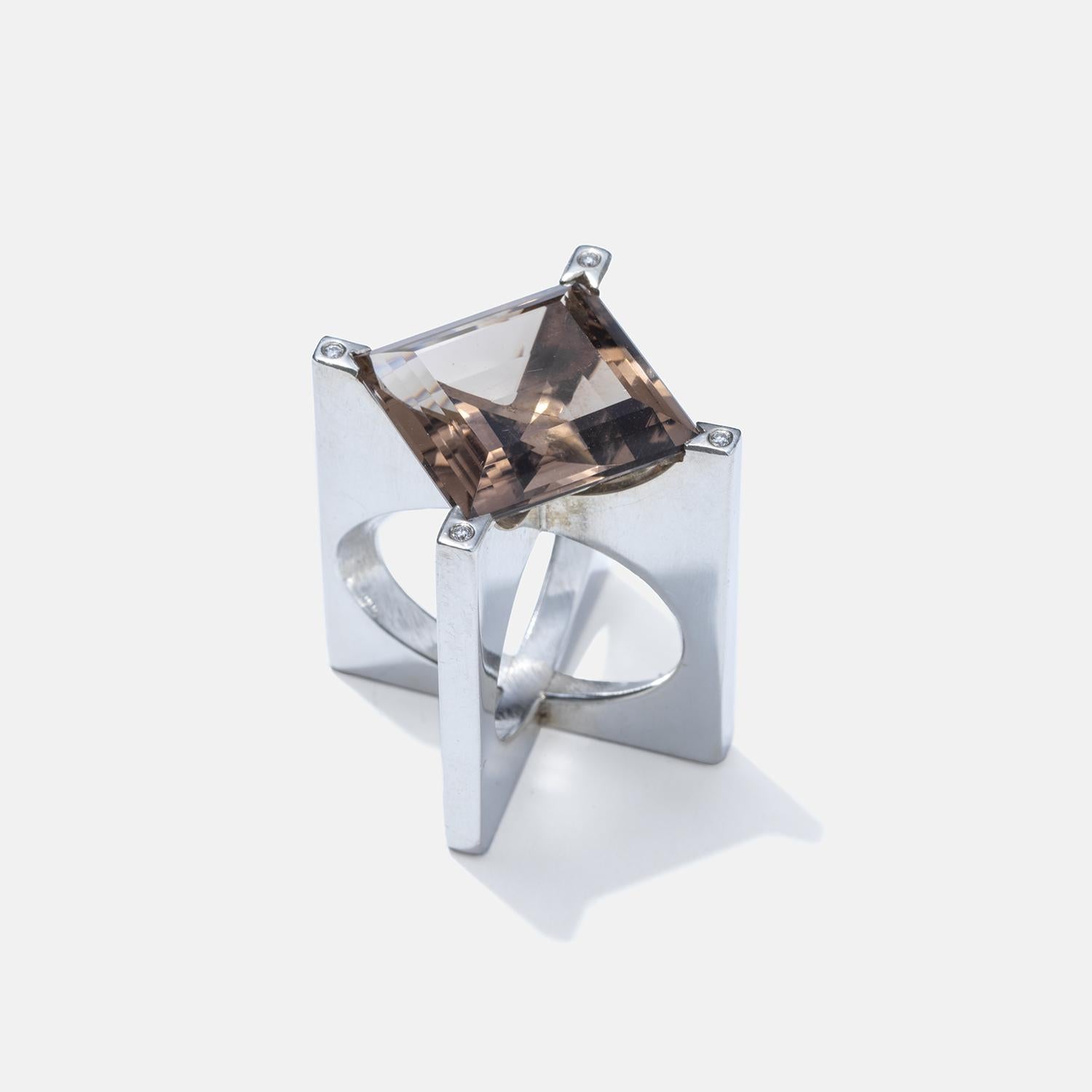 This ring features a bold, high-set design that elevates a large, square-cut smoky quartz at its center, showcasing a translucent brown colour. The silver band of the ring splits into four distinct, evenly spaced arms that support the high-set smoky