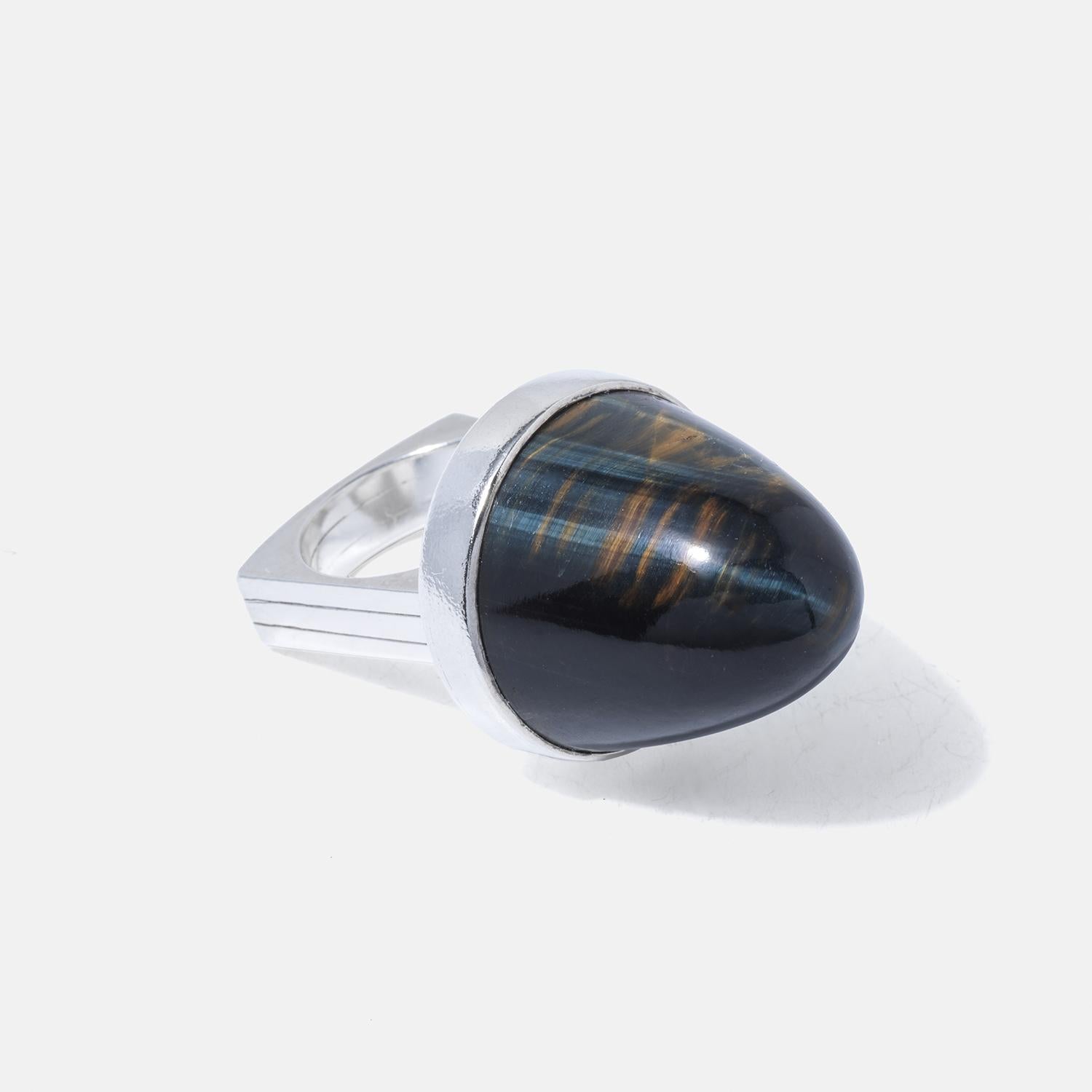 This striking ring features a cabochon-cut tiger's eye gemstone, set prominently atop a robust rectangular silver band. The stone's height accentuates its mesmerizing layers of golden and dark brown hues, which shift and shimmer with light. The