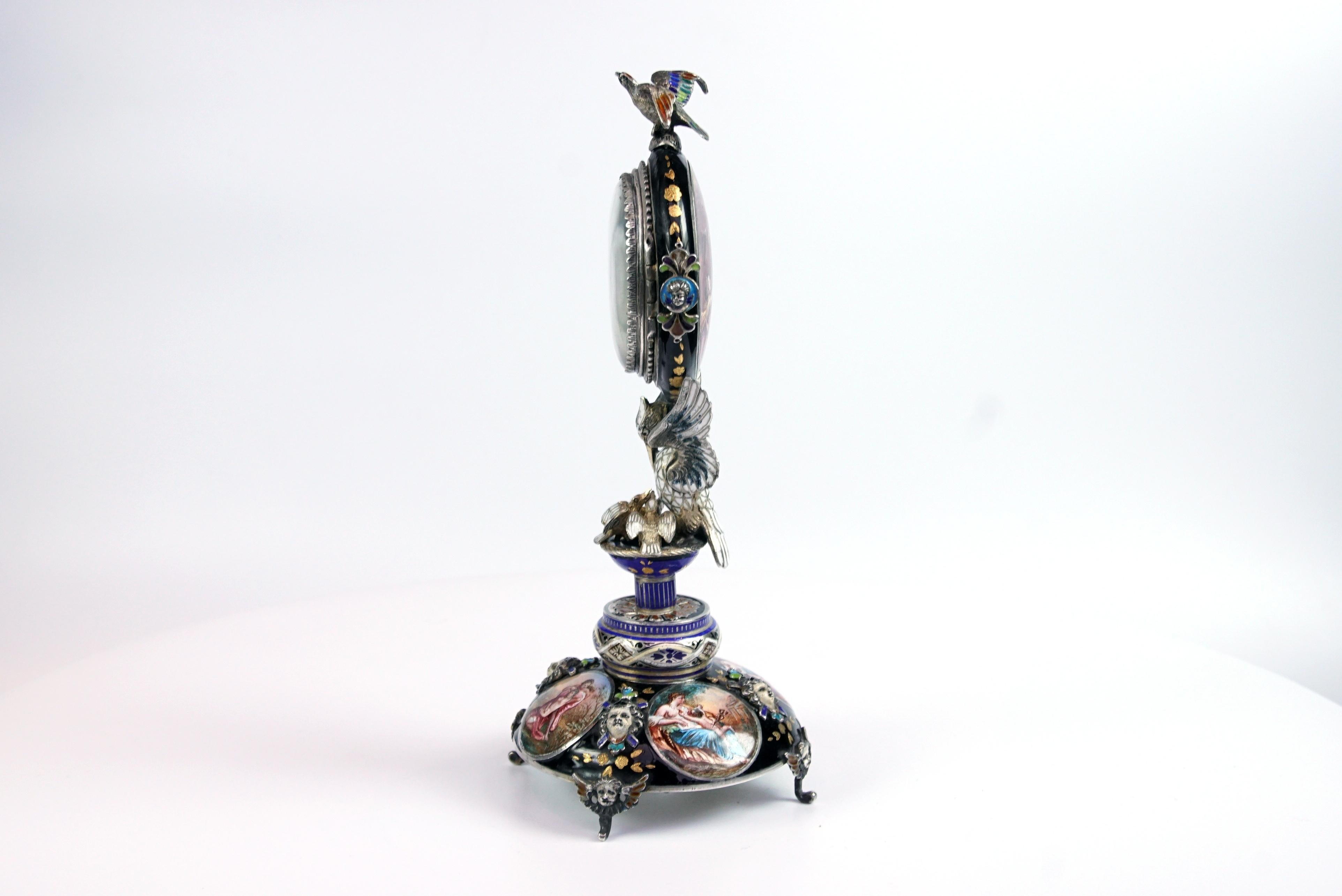 A fine silver and Viennese enamel clock with eagle by Hermann Bohm,

The highly painted clock supported by a pelican feeding her signets, the circular base with four vignettes of amorous couples, the interior painted with mythical scenes, the