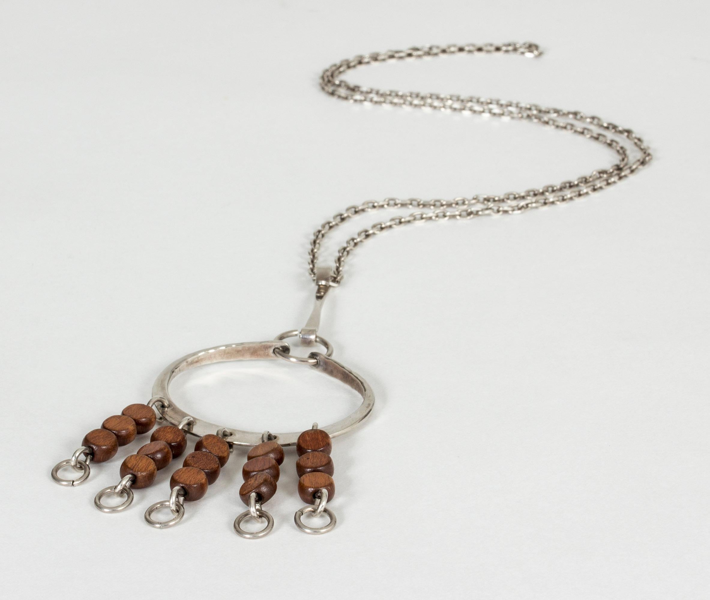 Beautiful silver pendant by Anna Greta Eker, with strands of brown wooden beads hanging loosely on silver chains. The large oval of the pendant has a gentle hand-hammered finish.