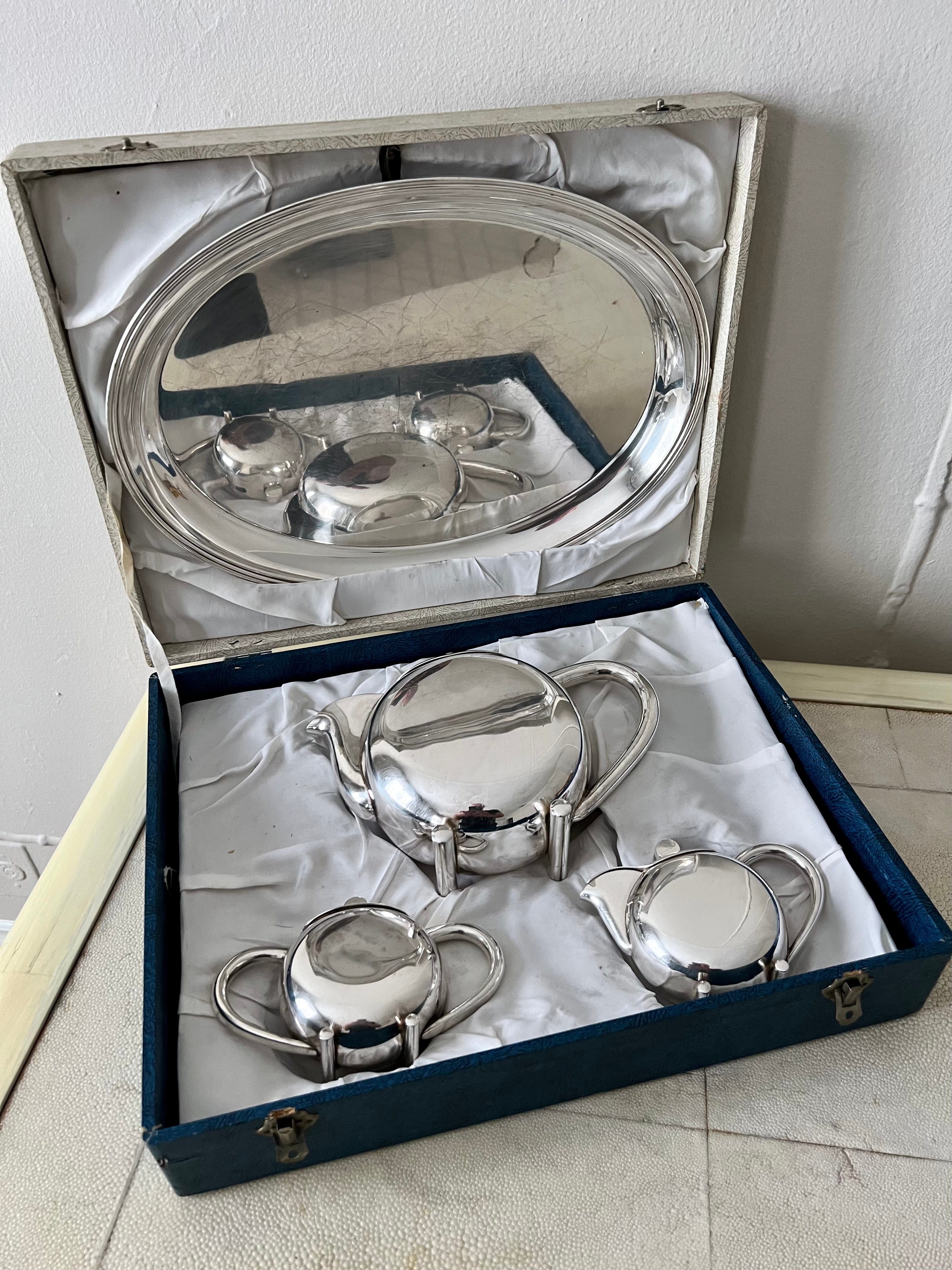 Silver tea set with tray, pot, cream canister, and sugar canister. The set comes in a blue and white double-clasp box for storage or transport. 

Catches light beautifully for a complement to any table or teatime. 

The dimensions listed are for