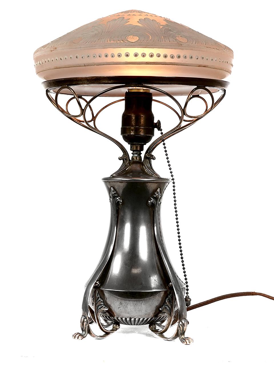 The base on this Art Nouveau lamp is silver plated with delicate scroll work. The glass shade is a unique floral pattern in a carved cameo style. The look is very rich.
