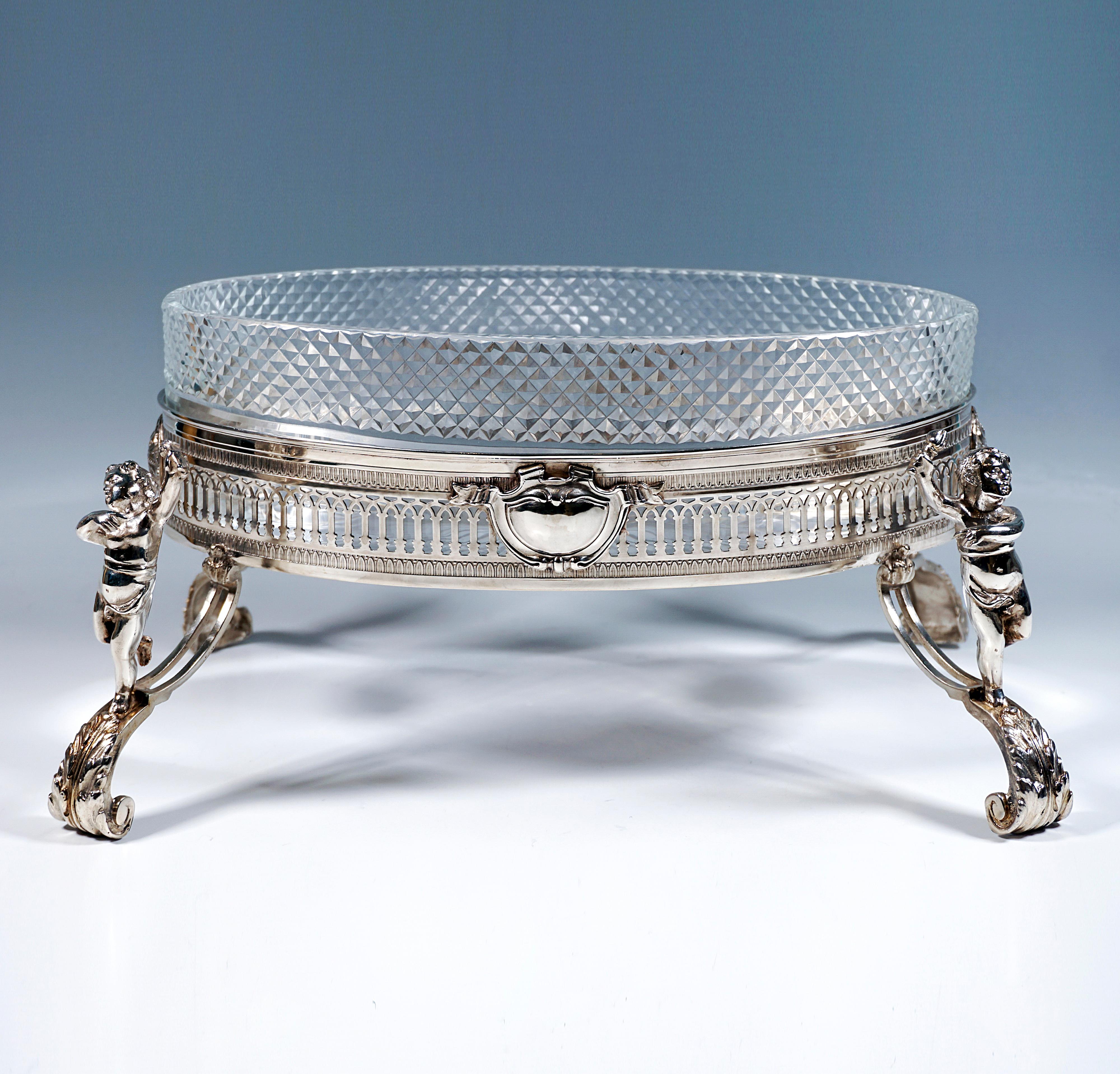 Eccezionale ed elegante jardinière in argento di forma ellittica su alte gambe a voluta ricurva con annessi putti completamente plastici come tedofori e poggiapiedi a foglia di piuma, vaso con parete verticale dritta e aperture regolari a forma di