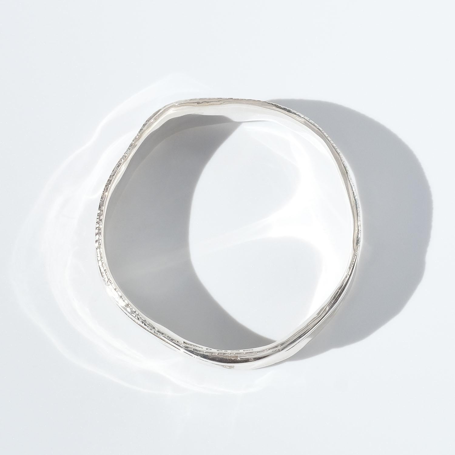 This sterling silver bangle bracelet has a glossy surface and irregular edges. It is decorated with silver flowing stripes.

The bangle will fit well in both an everyday environment as well as in a more festive one. This is what we would call a day
