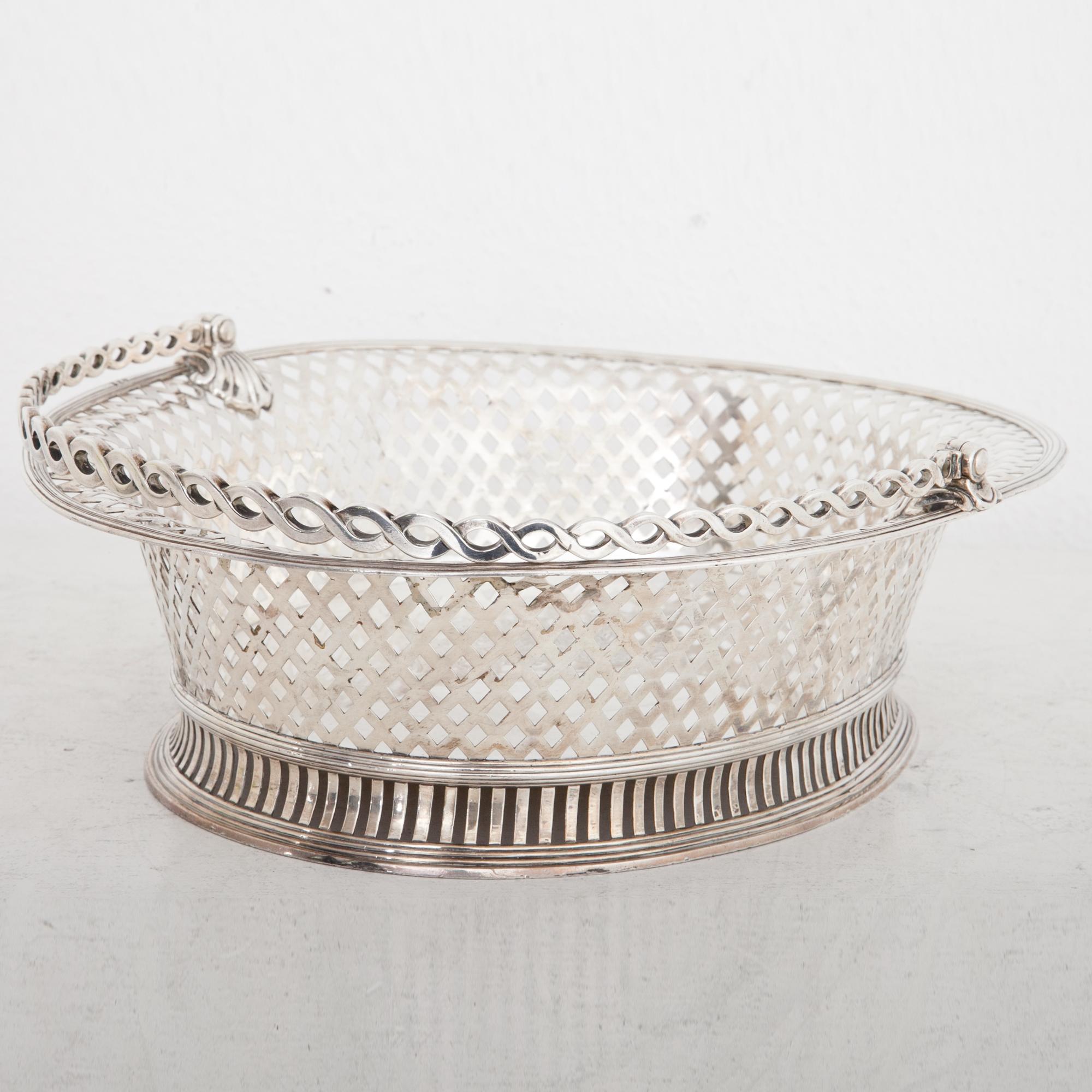 Oval silver basket with twisted handle and a pierced wall, staniong on a slightly broader stand with horizontal slats. The well shows a crowned coat of arms with a winged lion and a mounting horse as shield carries as well as a banner with the motto