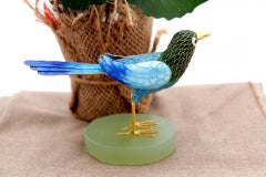 Silver bird covered in colored enamel on an elliptical stone base