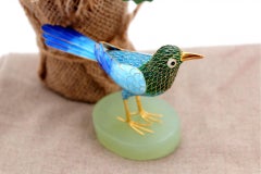 Silver bird covered in colored enamel on an elliptical stone base